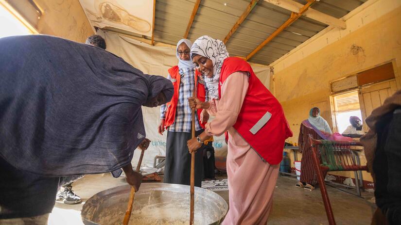 الممرضة المتطوعة في الهلال الأحمر السوداني وجدان حسن أحمد، مع متطوعين آخرين وأسر نازحة يقومون بإعداد وجبة في مخيم للنازحين في بورتسودان، السودان. 