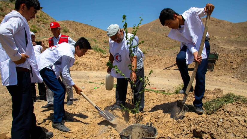 Tajikistan Red Crescent volunteer Azambek Dusyorov (left, holding shovel) joins several other Tajikistan Red Crescent volunteers in planting trees so that their roots can help keep the earth masses in place and prevent the likelihood of landslides and mudslides.