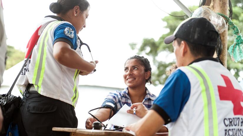 متطوعان في مجال الصحة في الصليب الأحمر الإكوادوري يقيسون ضغط دم امرأة في مستشفى متنقل في لاكوريرا، الإكوادور، ويستمعون إلى مخاوفها الصحية. 
