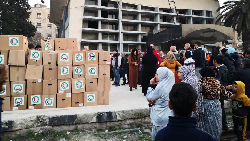 People affected by the earthquake in Syria line up to receive relief items sent in by the Iraqi Red Crescent Society. 