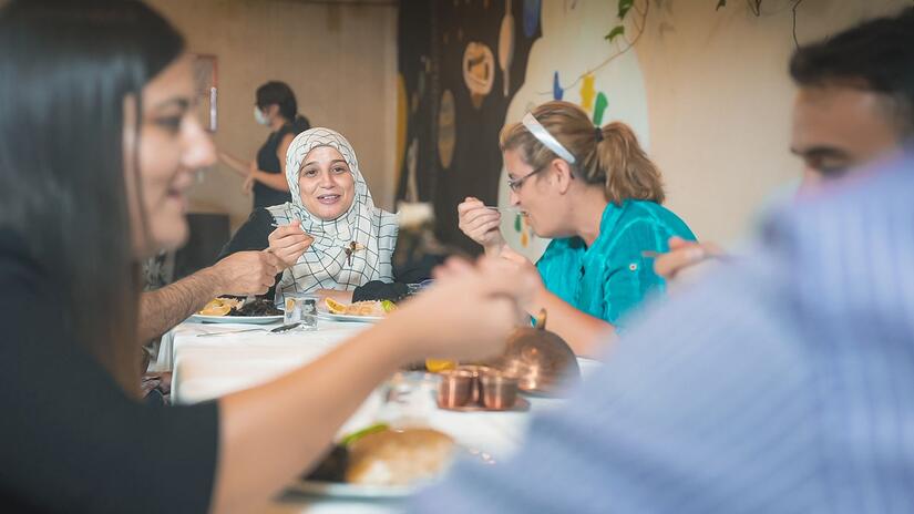 Houda sits and enjoys a meal with her fellow course companions and cooking teacher at a Turkish Red Crescent community centre.
