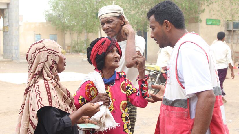 متطوع في الهلال الأحمر اليمني، أسامة، يتحدث إلى امرأتين أثناء توزيع المواد الغذائية.