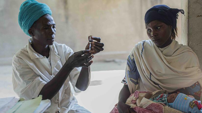 أم تراقب عاملة صحية في بونقور، تشاد، وهي تقوم بتطعيم طفلها. 