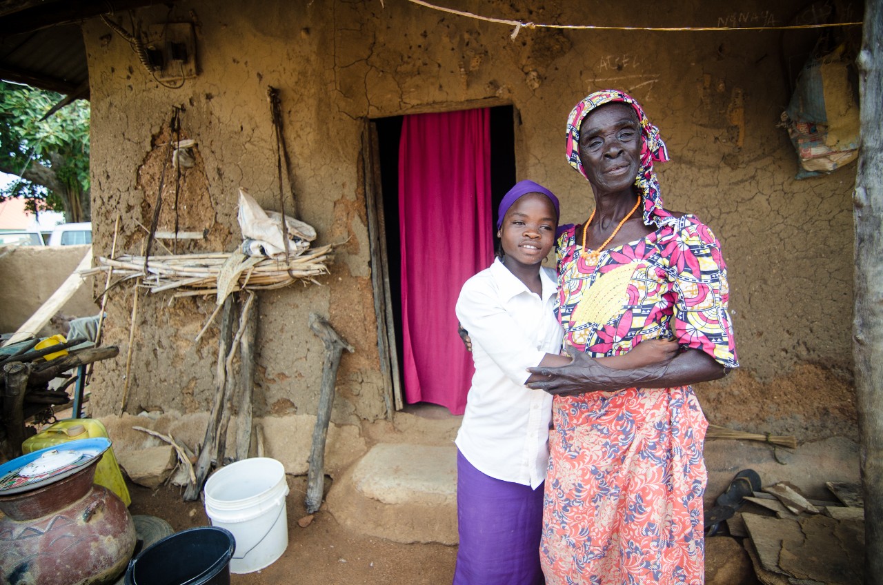 A girl stands with her grandmother outside her rural home in Nigeria