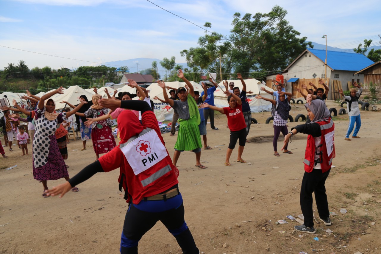 Indonesian Red Cross volunteers lead a psychosocial support session with people affected by an earthquake and resulting tsunami in Central Sulawesi. Support includes morning exercise sessions and readings of the Quran.