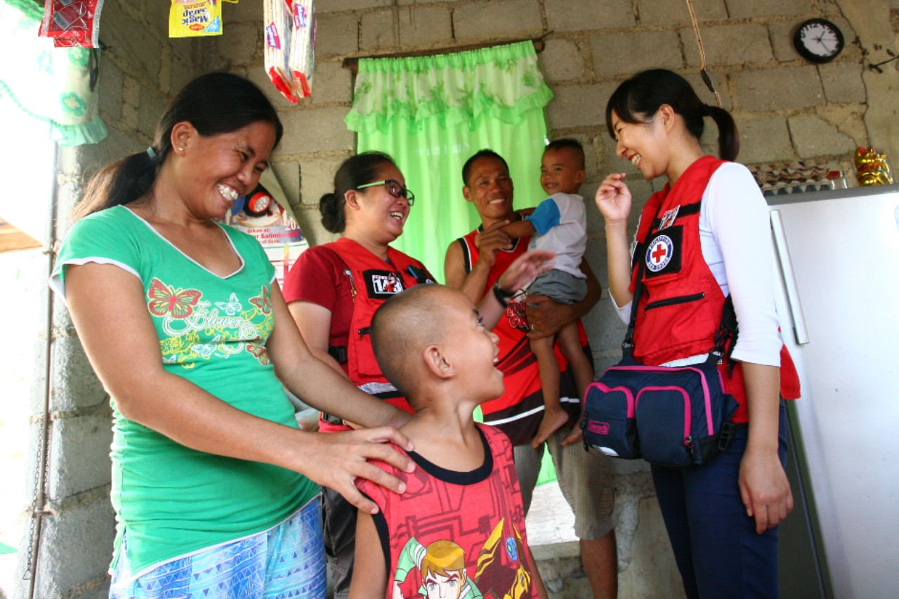 A family in Cebu, Philippines laugh and smile with Red Cross volunteers from the Japan Red Cross Society and Philippine Red Cross as they receive livelihoods assistance in 2015