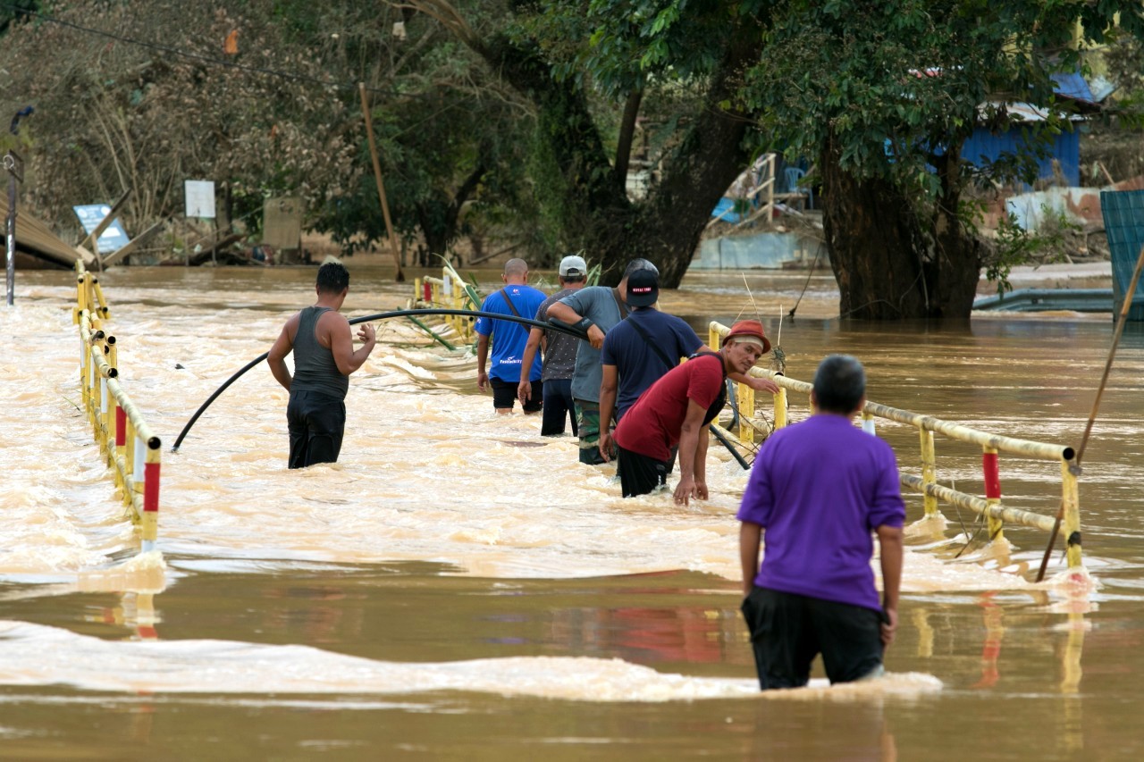 Des habitants de Terengganu, en Malaisie, tentent de traverser un pont menant à leur maison, qui a été submergée par des inondations dévastatrices au début de l'année 2021.