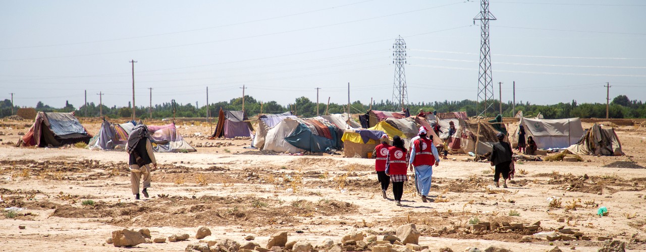 Voluntarios y voluntarias de la Media Luna Roja Afgana caminan hacia un pequeño campamento de desplazados internos en la provincia de Balkh, Afganistán, en el verano de 2021. La Media Luna Roja Afgana ha estado implementando un programa de transferencia de efectivo para ayudar a las personas a hacer frente a múltiples impactos, como la sequía, el COVID-19 y el conflicto. 