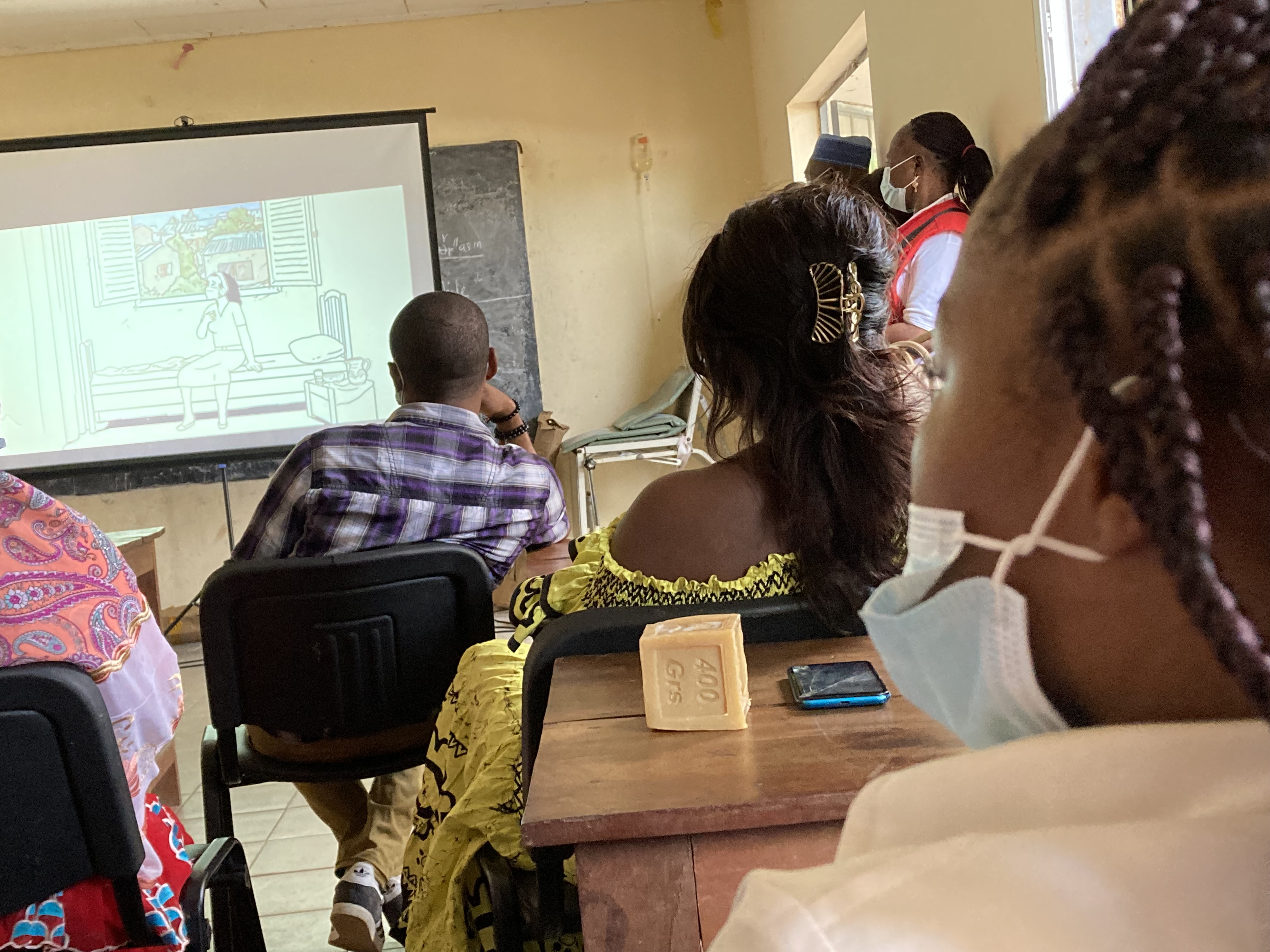 People stand in front of a projection screen and watch a short film on COVID-19 as part of the Community Programme for Epidemic and Pandemic Preparedness (CP3) project in the South Region of Cameroon. 