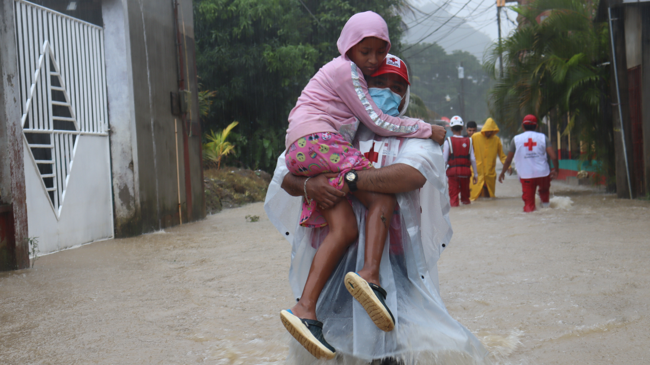A Guatemalan Red Cross volunteer carries a young girl through flood water to safety after Hurricane Julia tore through Central America in October 2022, bringing intense rains and flooding.