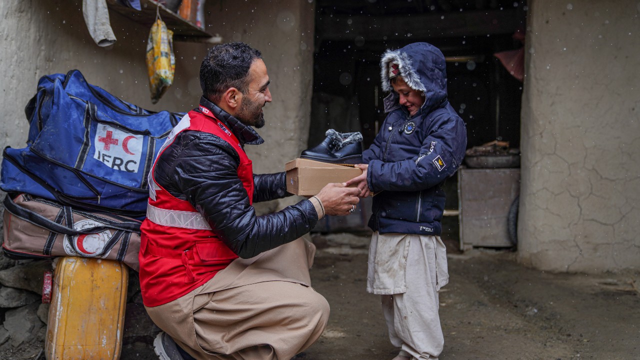 En enero de 2023, un voluntario de la Media Luna Roja Afgana entrega a un niño de la provincia afgana de Paktika un nuevo par de zapatos de invierno para ayudarle a mantenerse abrigado durante el crudo invierno. La Media Luna Roja Afgana, con el apoyo de la IFRC, está proporcionando a las comunidades de la región kits de invierno para ayudarles a sobrellevar la situación.