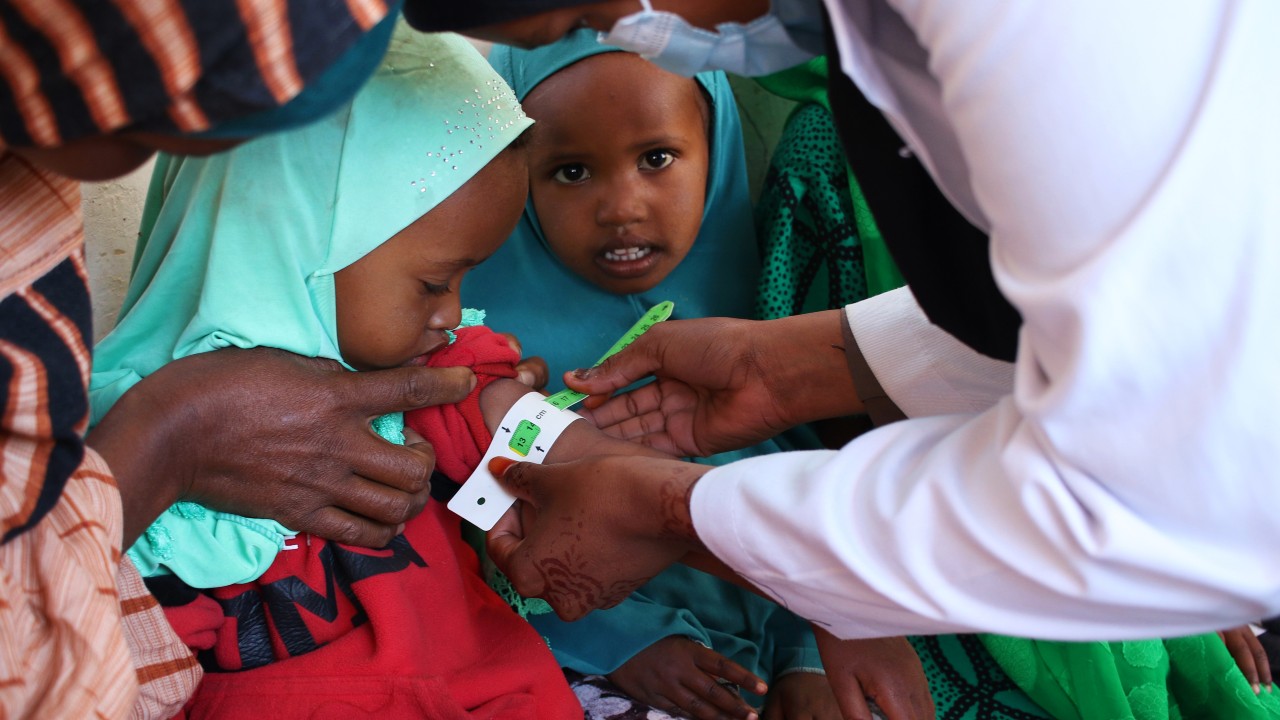 Nimco, a young Somali girl, watches as her friend, Dheeman, has a Mid-Upper Arm Circumference (MUAC) band measurement as part of her screening for malnourishment at a Somali Red Crescent Society Clinic in February 2023.