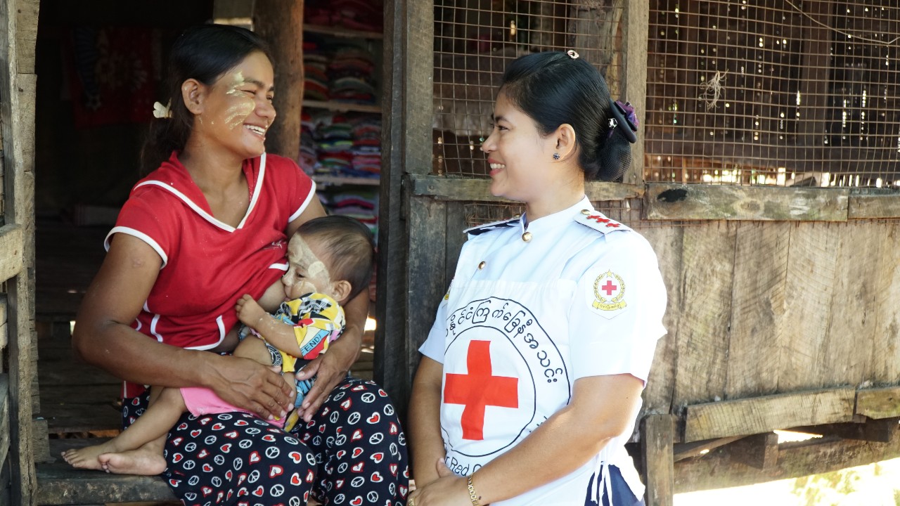 Moe Thuzar, a woman from Kyaik Kha Me Township, Myanmar, holds her son as she smiles at Myanmar Red Cross ambulance volunteer Thi Thi Mon who had helped rush her to hospital when she was giving birth.