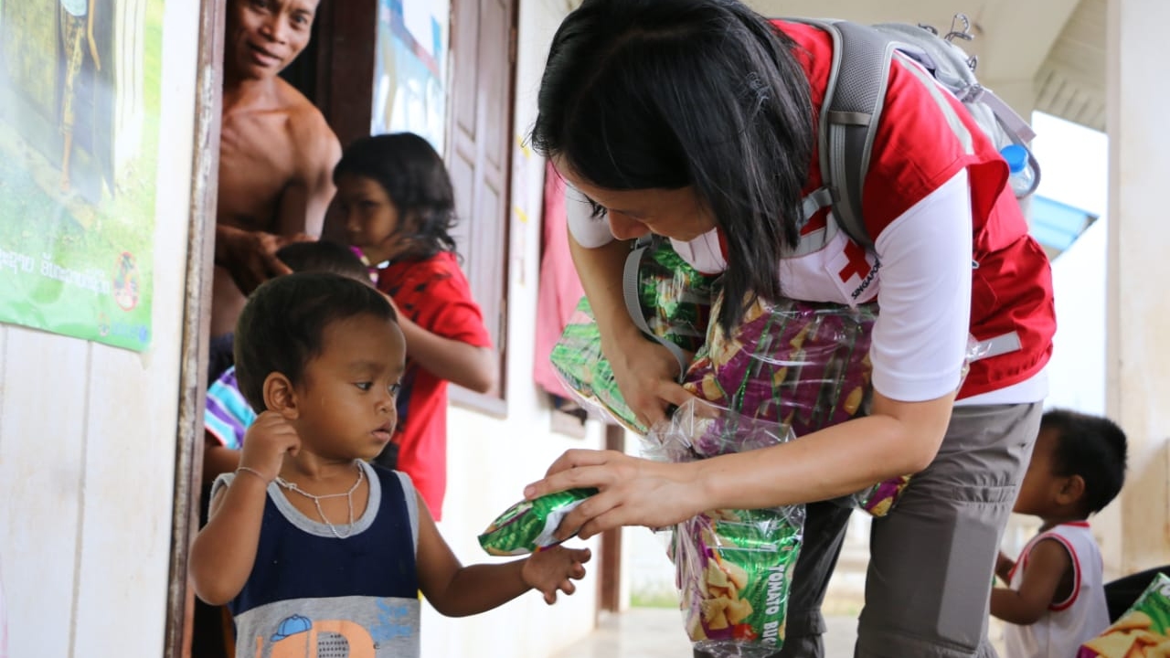 A Lao Red Cross volunteer offers food to a young boy in Baan Saeng Chan, Laos, whose family was affected by flash flooding when a dam collapsed in 2018.