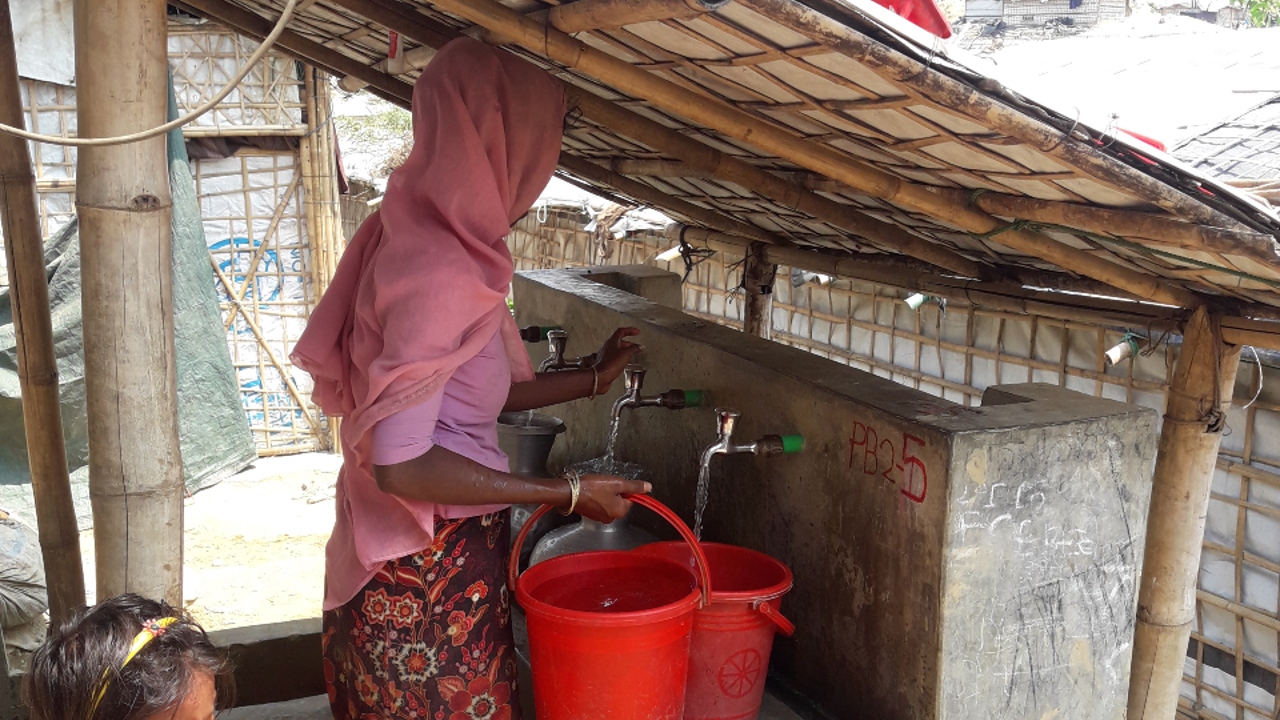 A woman in Cox's Bazaar camp collects clean drinking water in a bucket from a water point installed by the Bangladesh Red Crescent.