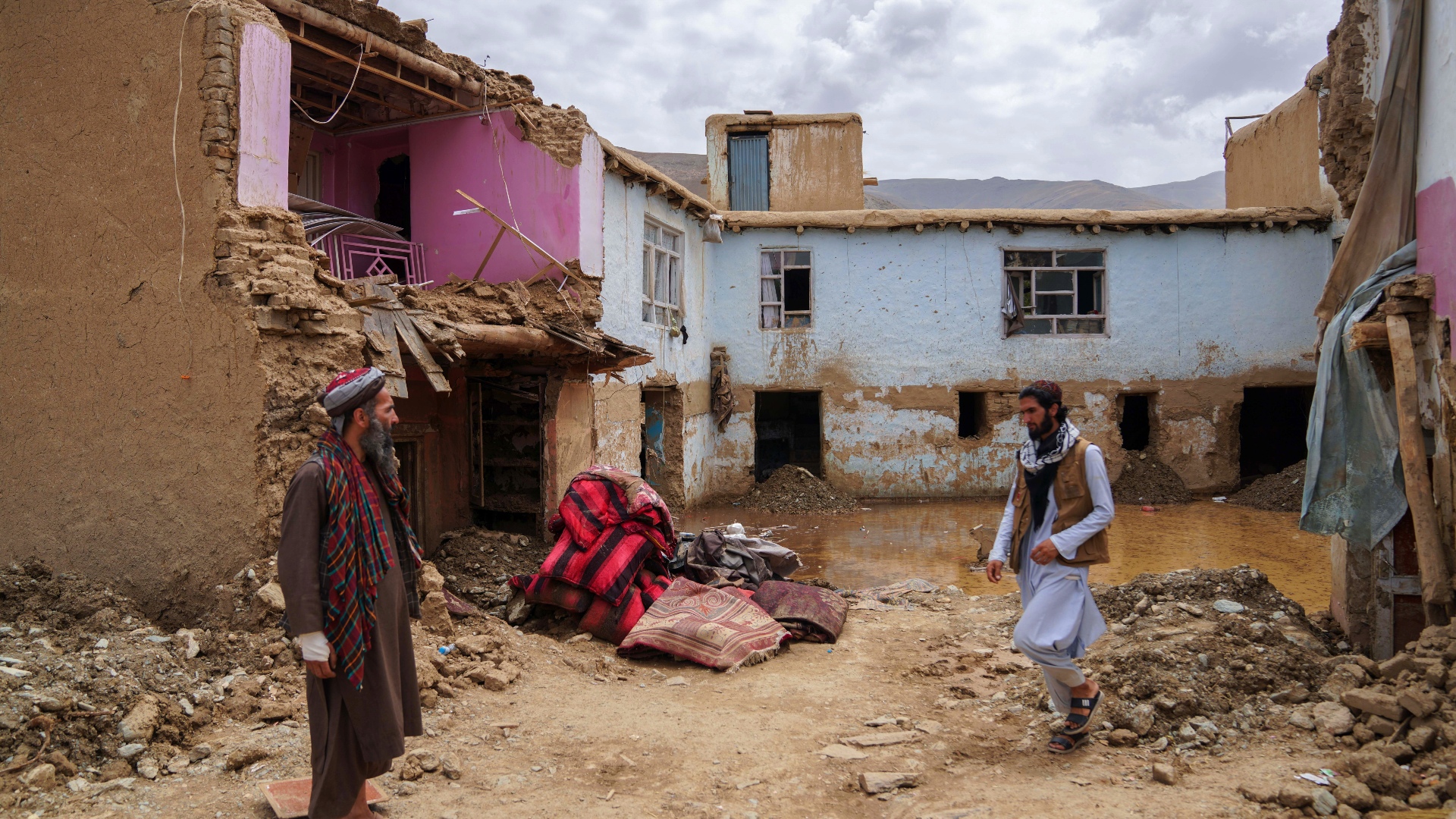 Two men stand in front of buildings damaged by flooding in Afghanistan in late July 2023.