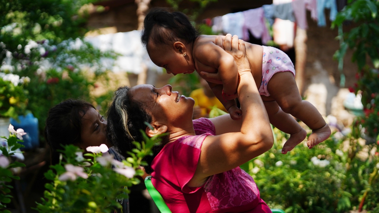 Rosa sonríe con su nieta en brazos frente a su casa en el oeste de El Salvador.