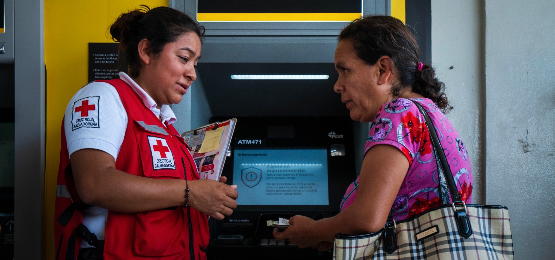 Una voluntaria de la Cruz Roja Salvadoreña ayuda a Rosa, del oeste de El Salvador, a sacar dinero de un cajero automático para ayudarla a ella y a su familia a hacer frente al terremoto de enero de 2023.