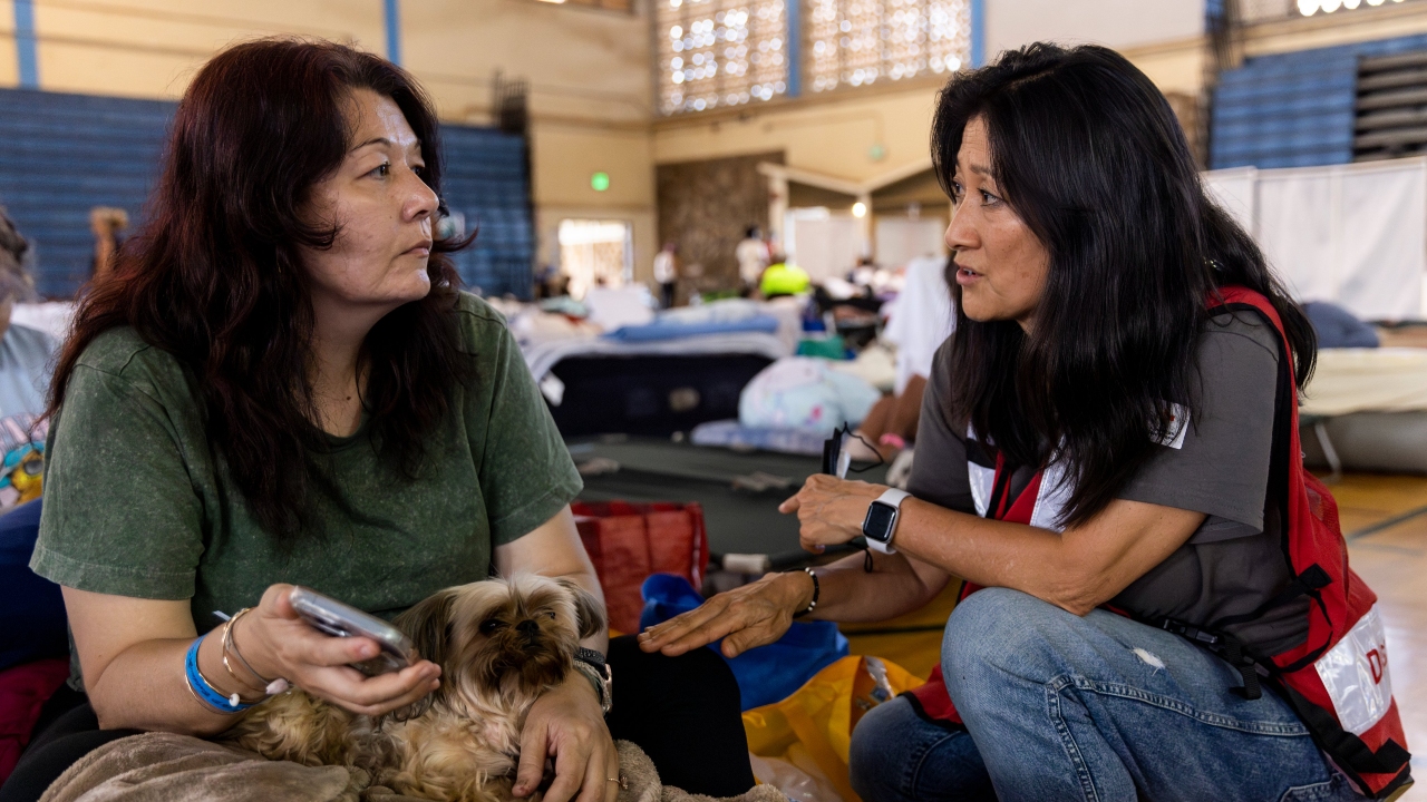 En un refugio de la Cruz Roja, una voluntaria de la Cruz Roja consuela a una mujer que escapó con dificultad de Lahaina con sus tres hijos y su perro durante los incendios de Maui.