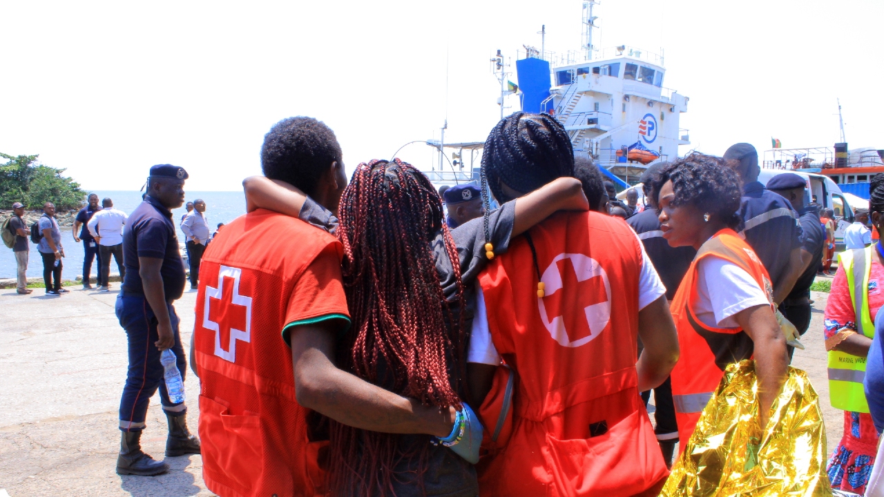 Two Gabonese Red Cross volunteers support a woman rescued from the capsized Esther Miracle ferry in Gabon to walk as they escort her to a waiting ambulance.