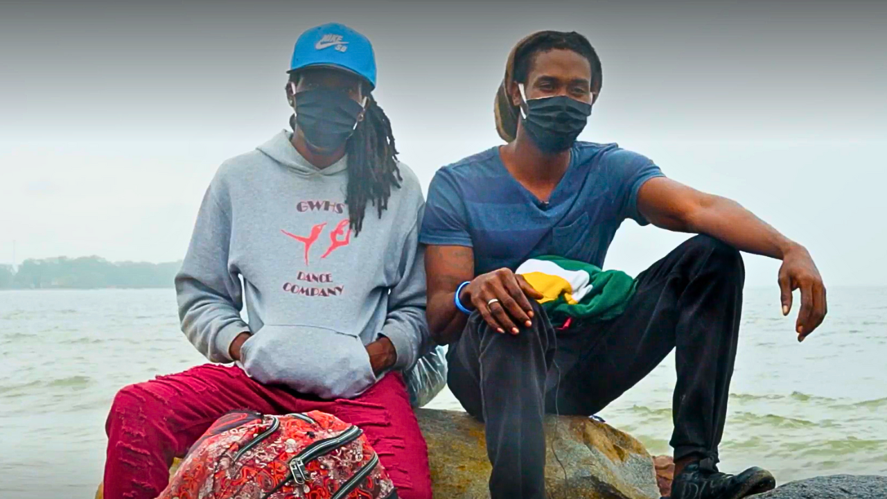 Brothers Máximo and George sit on a rock with their backs to the sea at the Centre for Attention to Returned Migrants (CAMR) in Honduras.