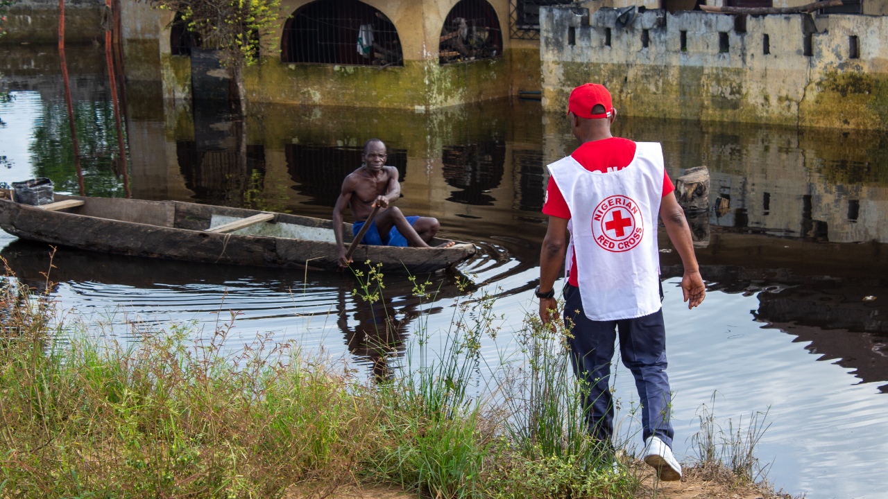 A Nigerian Red Cross volunteer approaches a man using a wooden boat to get around his community in Ahoada, Nigeria during widespread flooding in November 2022.