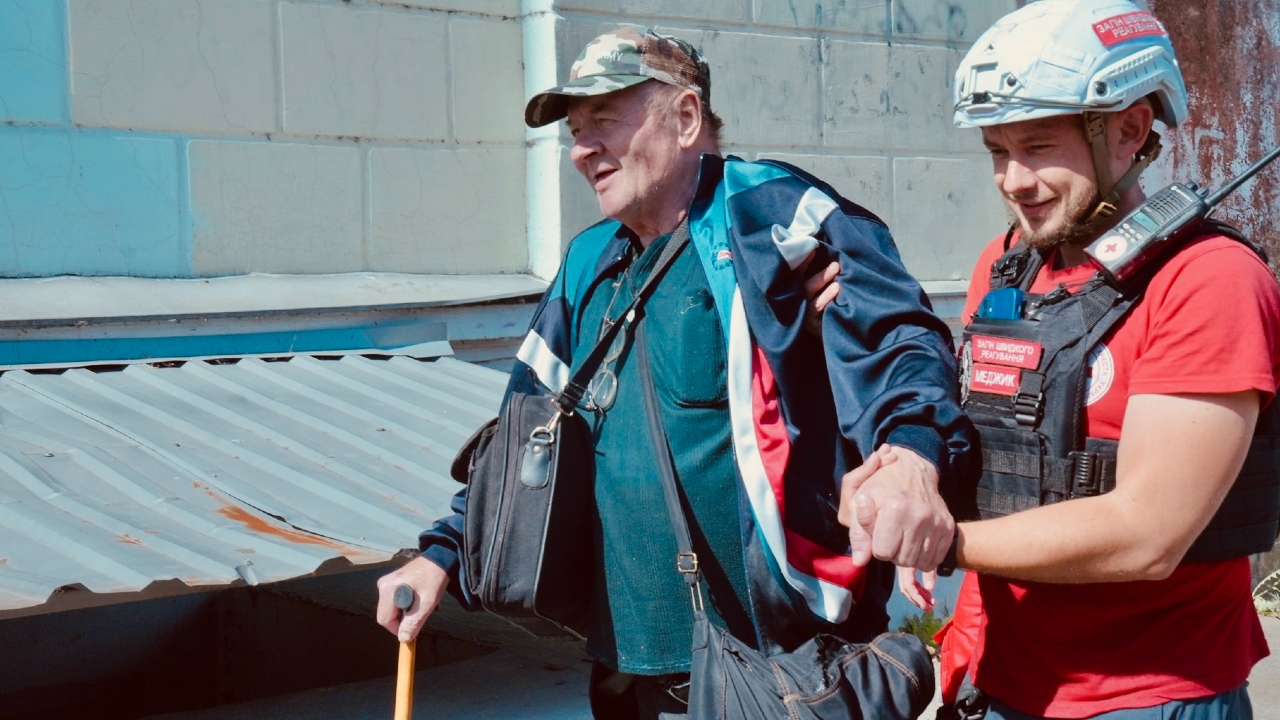 A Ukraine Red Cross Society rescue volunteer supports a man with a walking stick to escape flooding caused by the Kakhovka Dam collapse in June 2023.