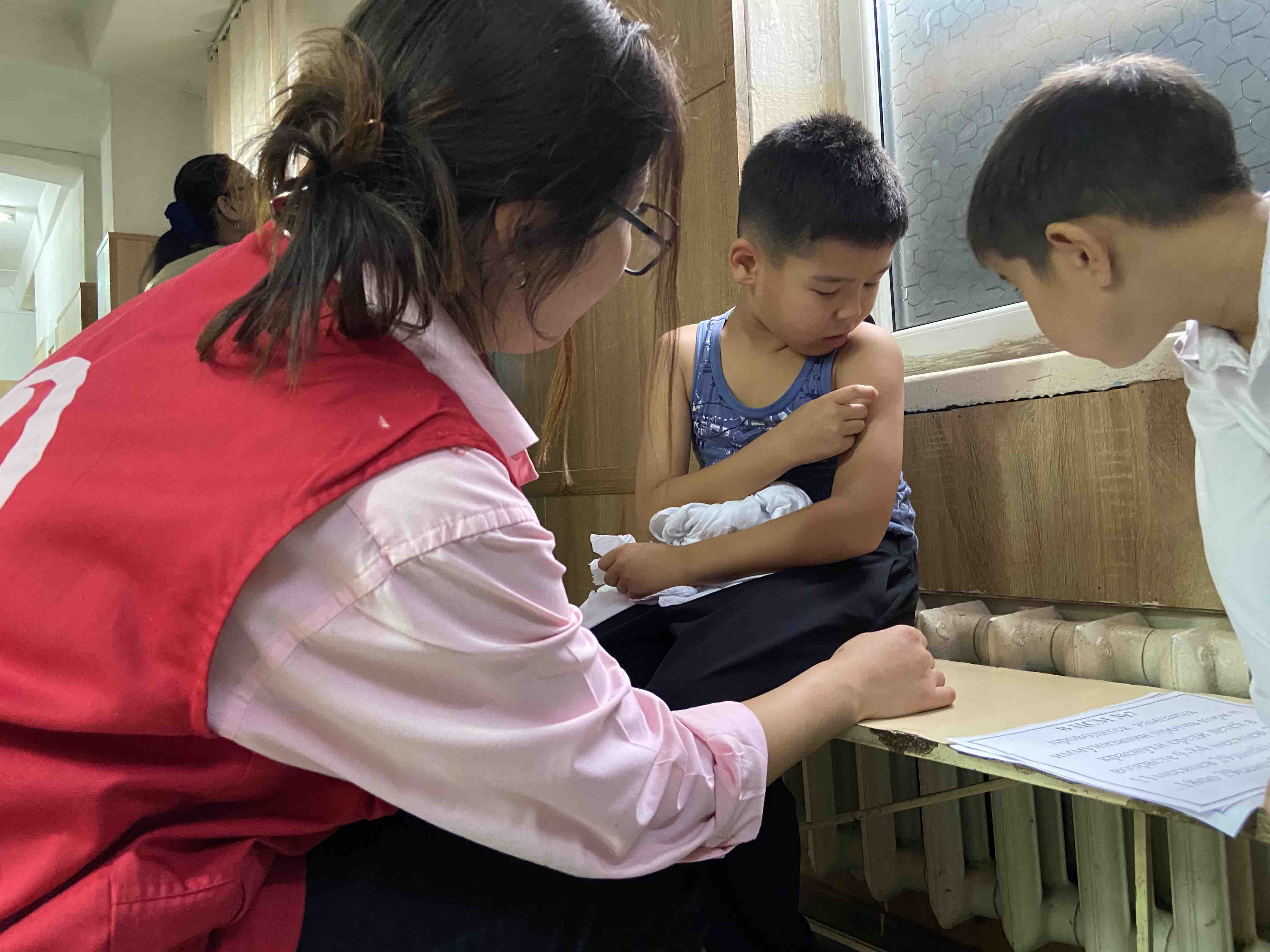 A Kyrgyzstan Red Crescent volunteer administers a measles vaccine to a young boy.
