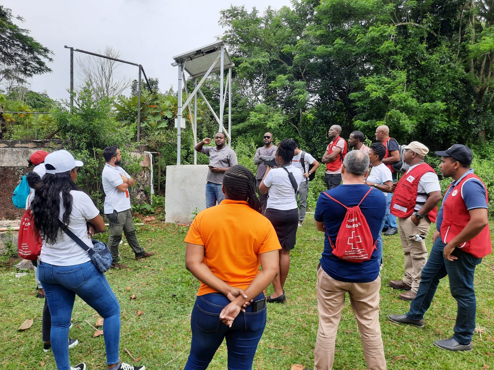 Red Cross staff and volunteers from across the Caribbean listen to representatives from Konnexx Services Ltd. explain how the solar powered water pump (in background) works, during a field trip to the Caribbean Christian Centre for the Deaf (CCCD).