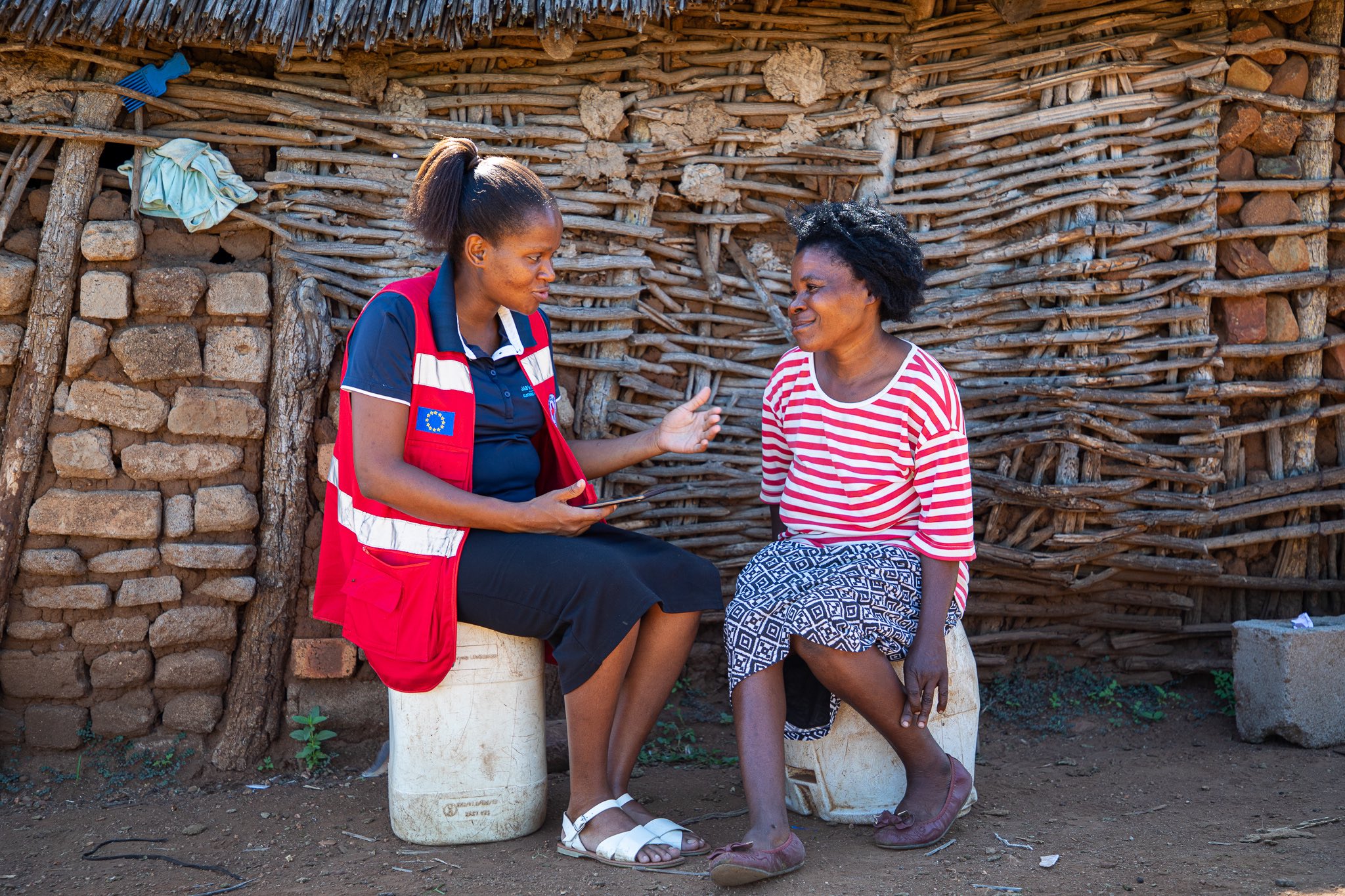 Baphalali Eswatini Red Cross Society volunteer Bethusile Nxumalo speaks with 44-year-old Winile Masuku outside her home.