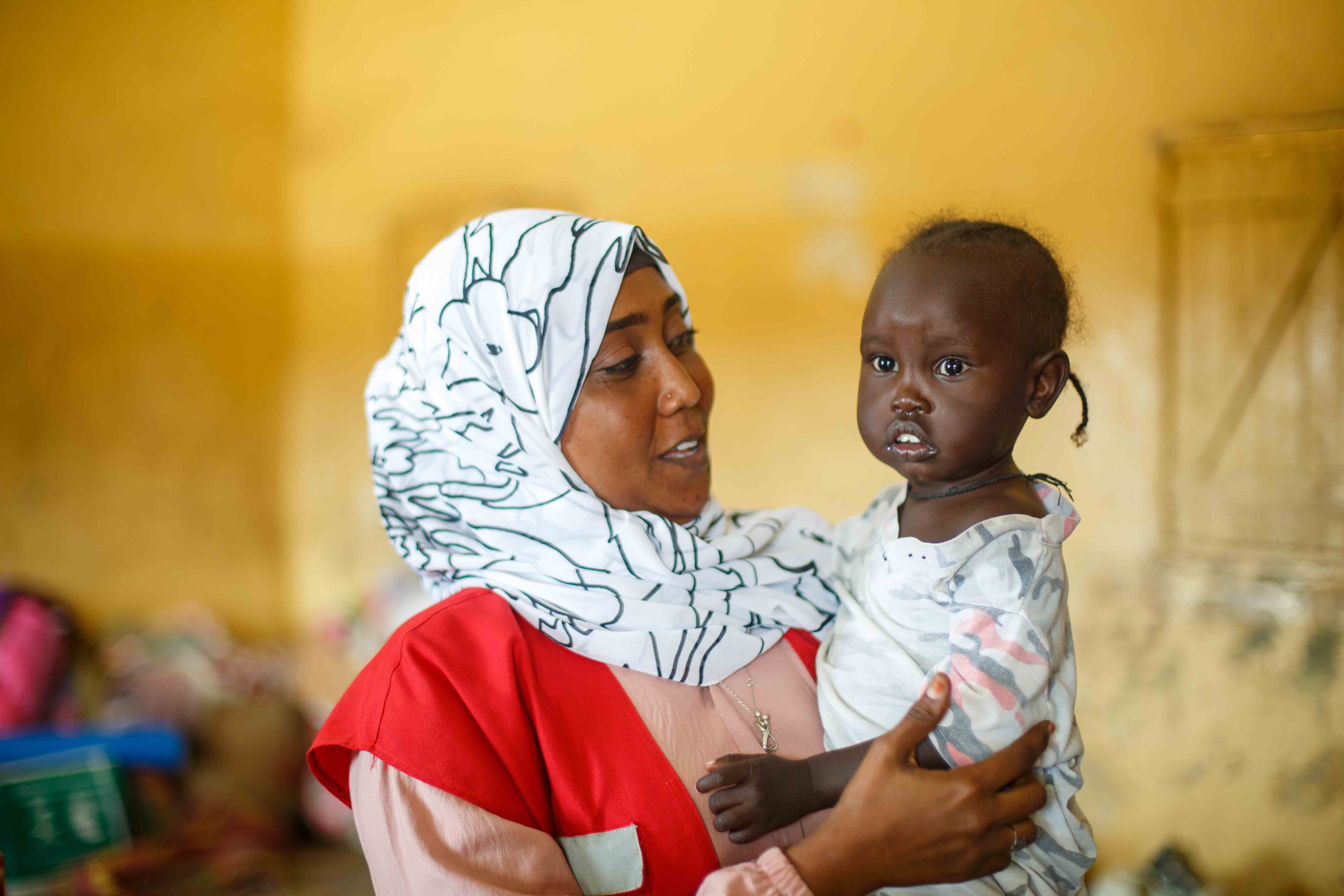 Wajdan Hassan Ahmed, a volunteer with the Sudan Red Crescent Society, holding a young child during a visit at a camp for internally displaced persons in Port Sudan. 