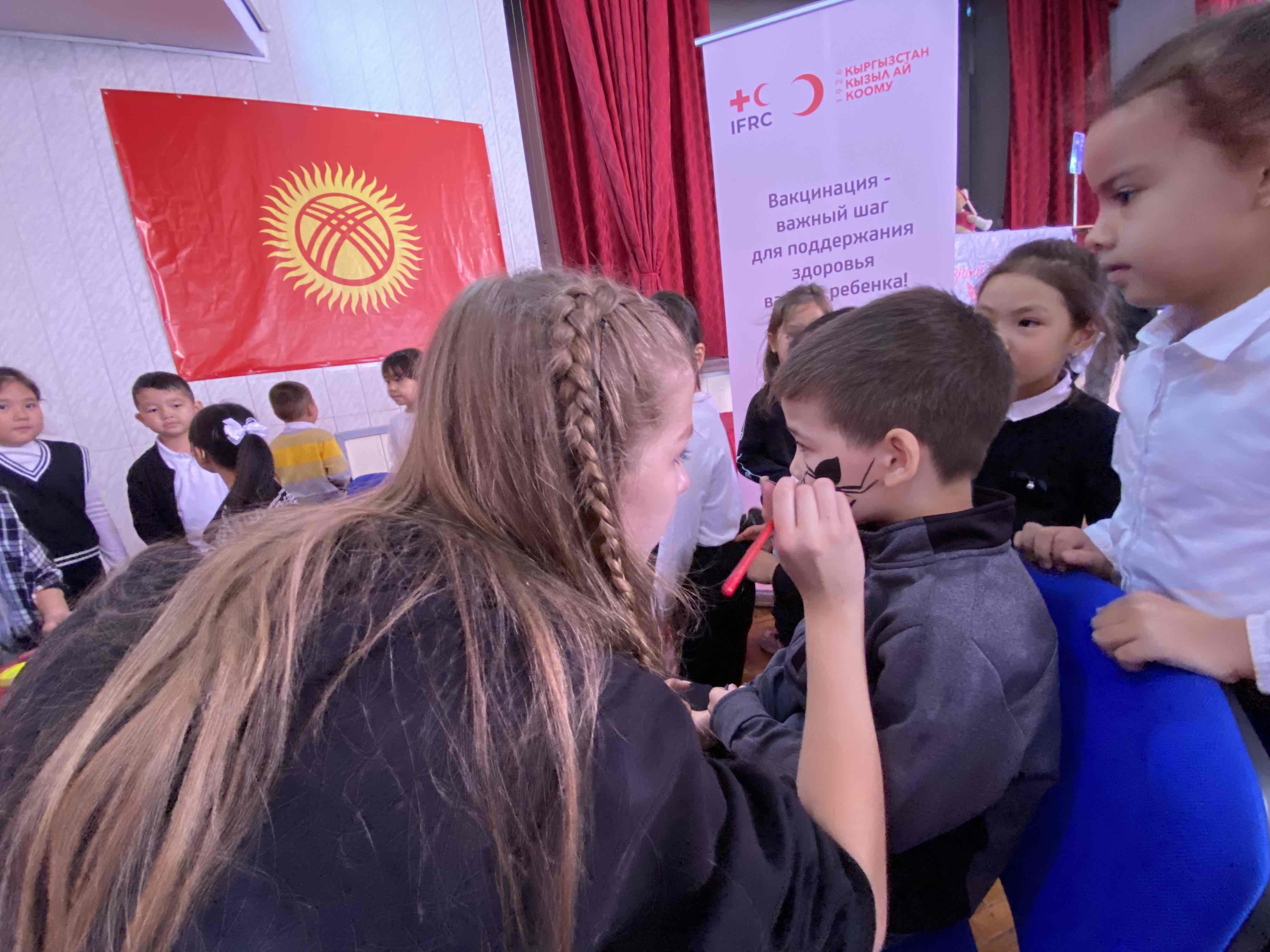 At a vaccination station for young children, a Kyrgyzstan Red Crescent volunteer paints a spider on a boy’s face as part of an immunization drive in response to a measles outbreak.