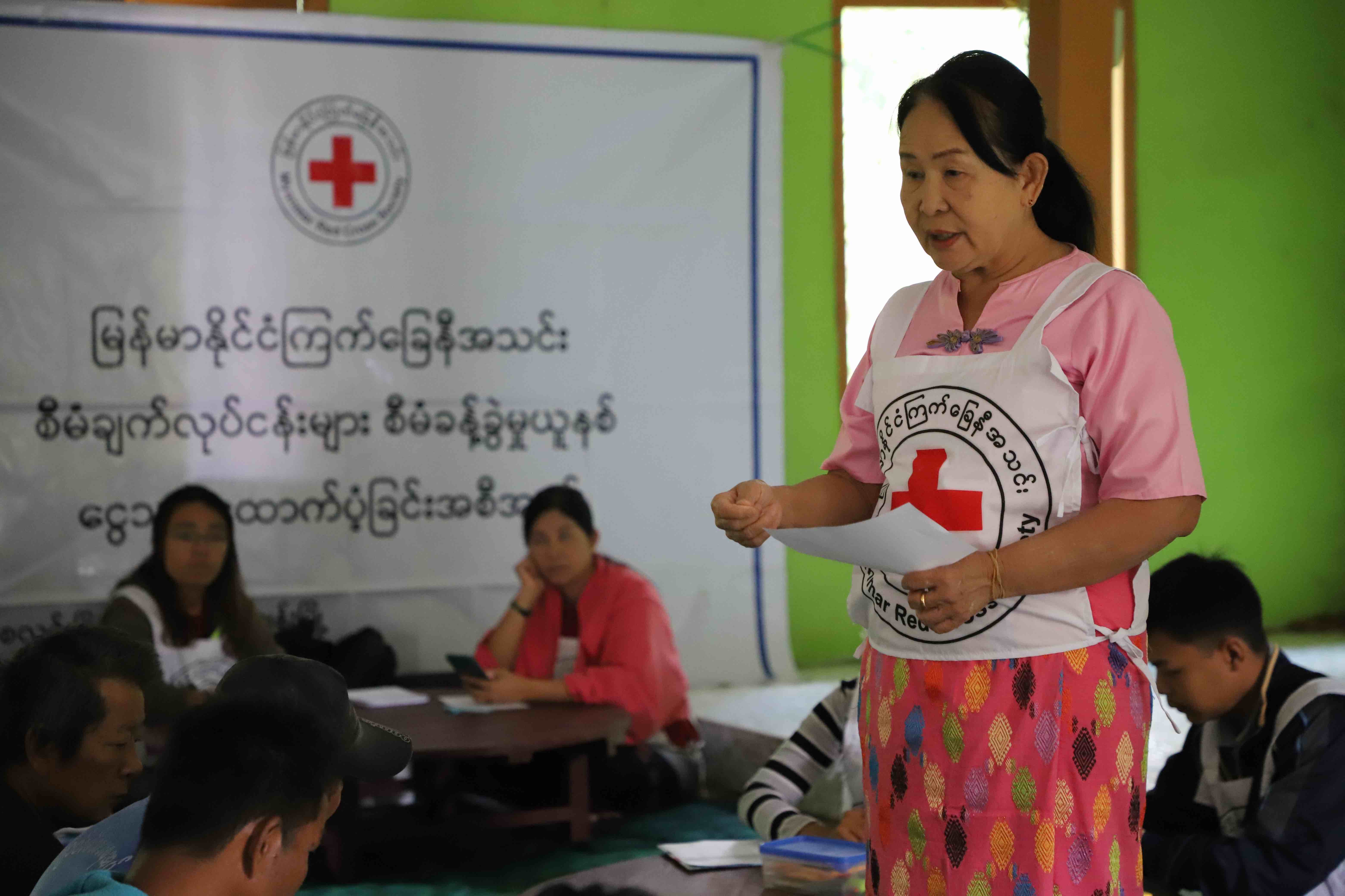 Dr. Chaw Khin talks with people impacted by Cyclone Mocha in 2023 about the Red Cross and its Fundamental Principles, just prior to a cash distribution aimed at helping people get back on their feet. 