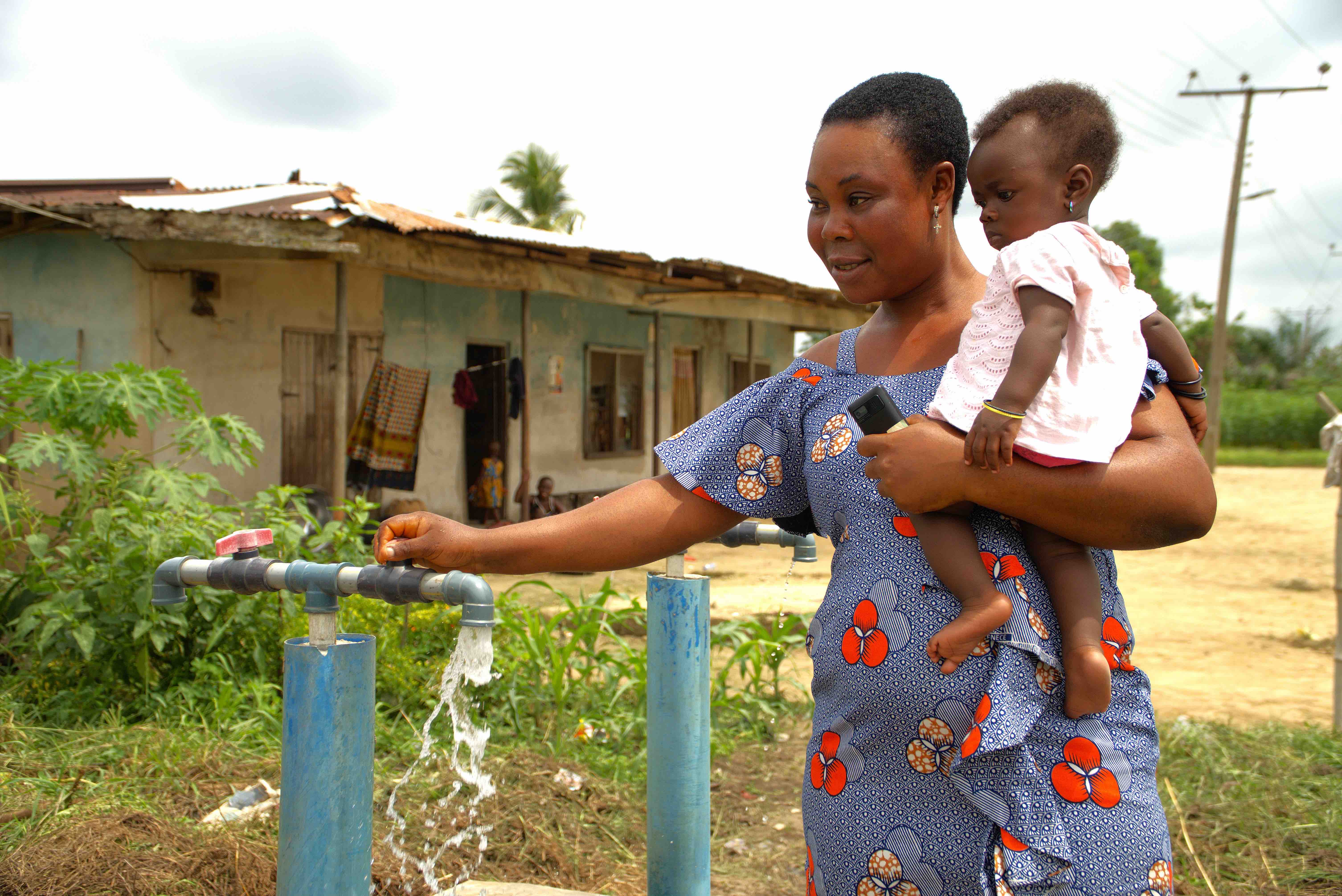 Blessing Emeldi holds one of her children as she gets water from a newly established water point in Nigeria’s Ivrogbo-iri community, which was hard hit by devastating floods in 2022. Those floods washed away Emeldi’s farm and her crops of bananas, yams and cassava. 