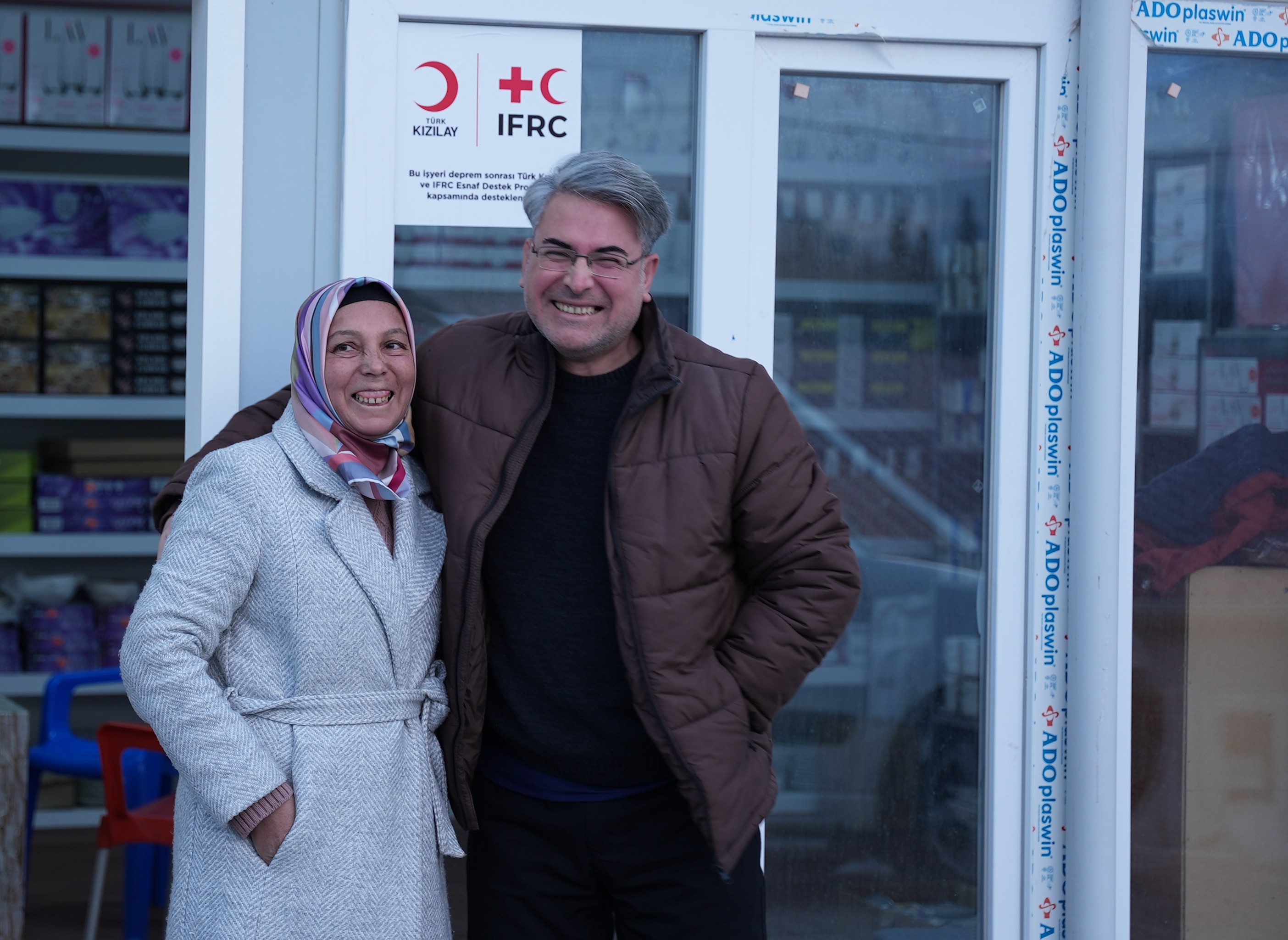 Döndü and Yavuz stand in front of her glassworks business, which was almost completely destroyed by the February 2023 earthquakes. Small grants from the IFRC and Turkish Red Crescent have helped her rebuild her business. 