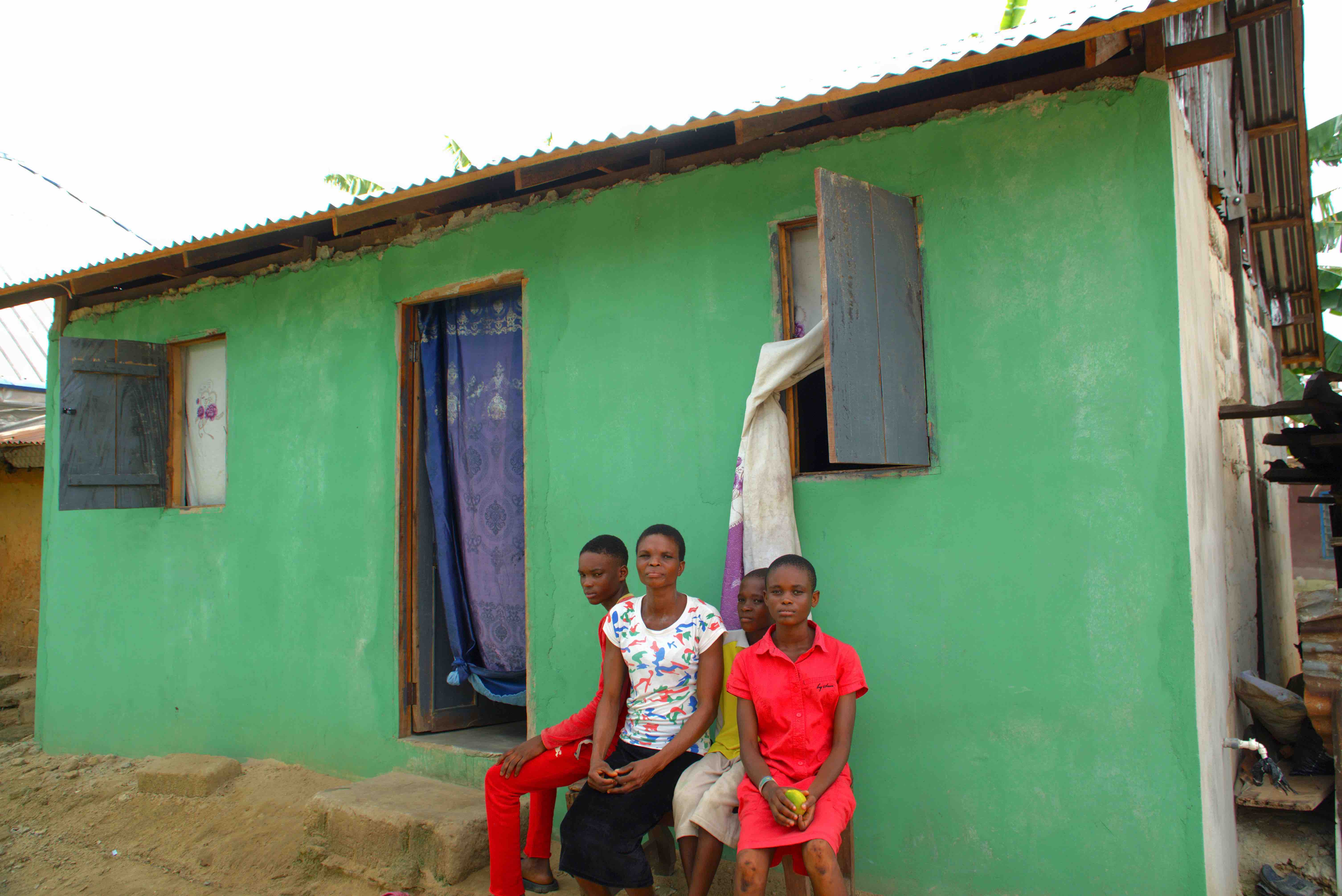 Gladys Ajiri (center) sits with three of her children in front of her new home, built using concrete blocks. Her earlier home, made from traditional mud construction, was washed away by the floods in 2023.