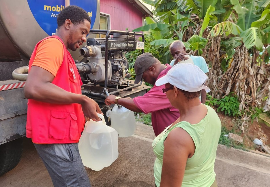 A Grenada Red Cross volunteer helps residents fill water bottles from the back of a water truck in order to help people cope with extended drought and prolonged heatwaves.