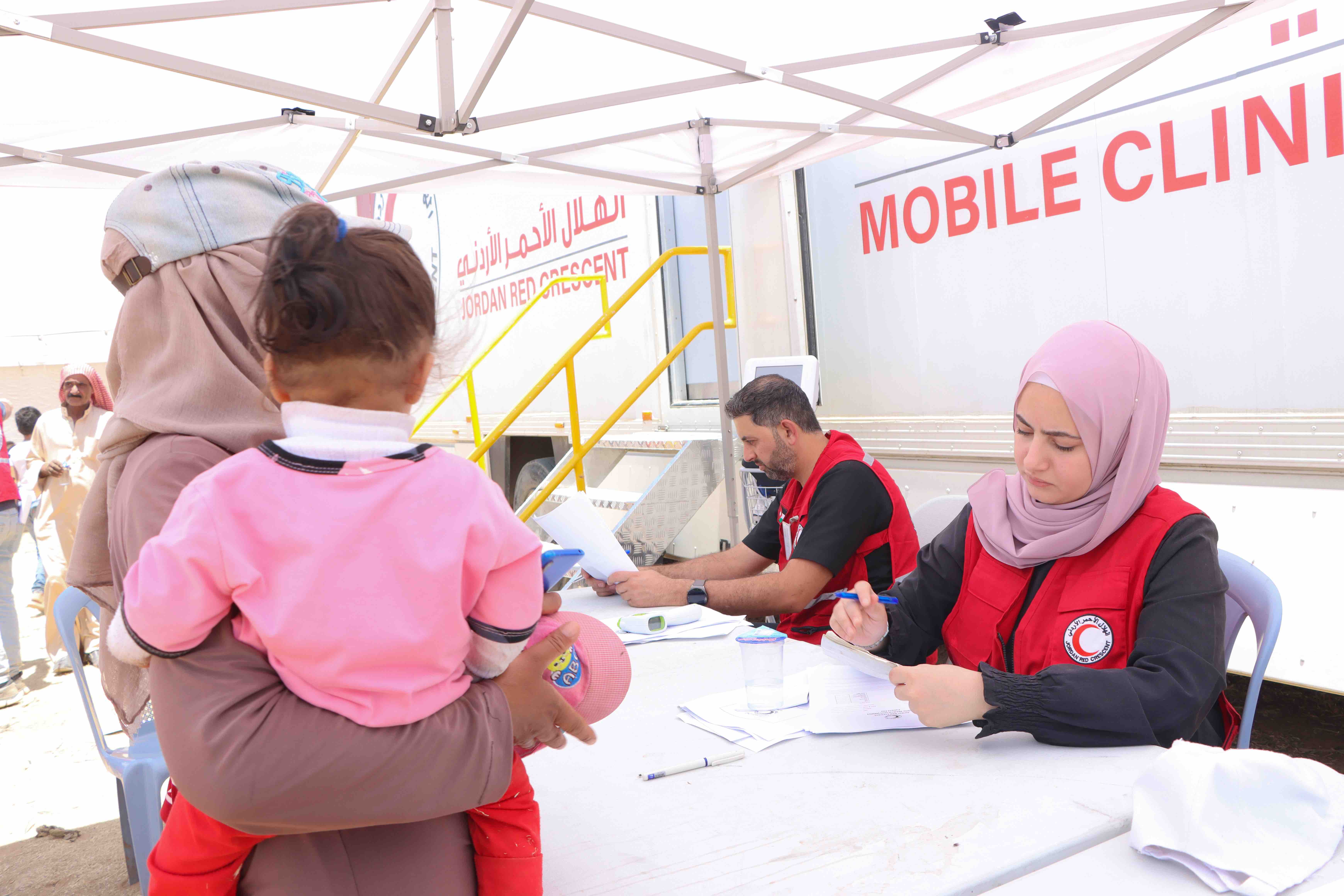 امرأة وطفلها يتلقيان المساعدة الطبية من عيادة صحية متنقلة تابعة للهلال الأحمر الأردني في مخيم اللبن.