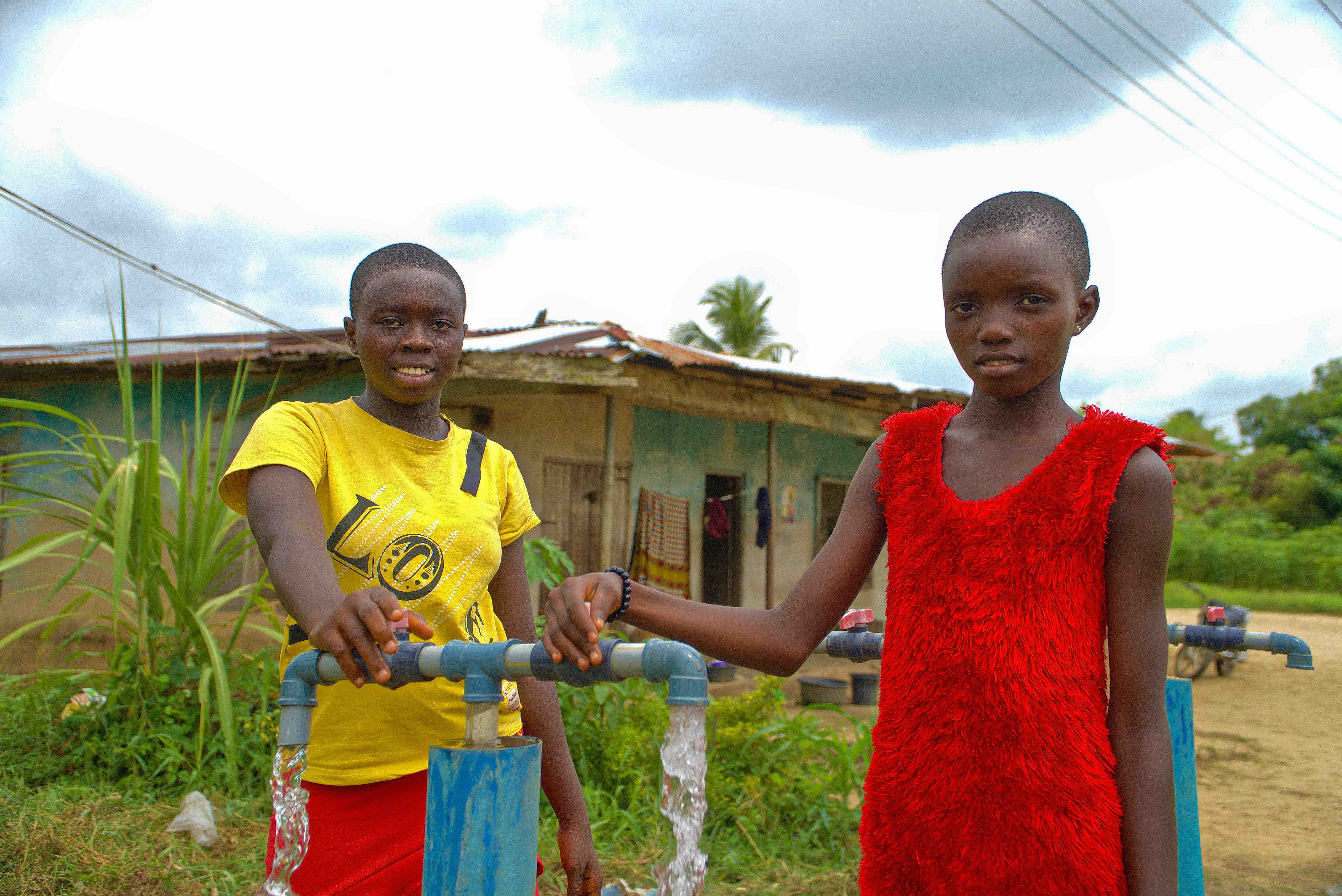 Two sisters, Juliet and Constance Elorghor, gather water from a new water source established by the Nigerian Red Cross in their community after floods in 2023.  14-year-old Juliet and 9-year-old Constance say the ready availability of water means they spend less time going to get water and more time in school.