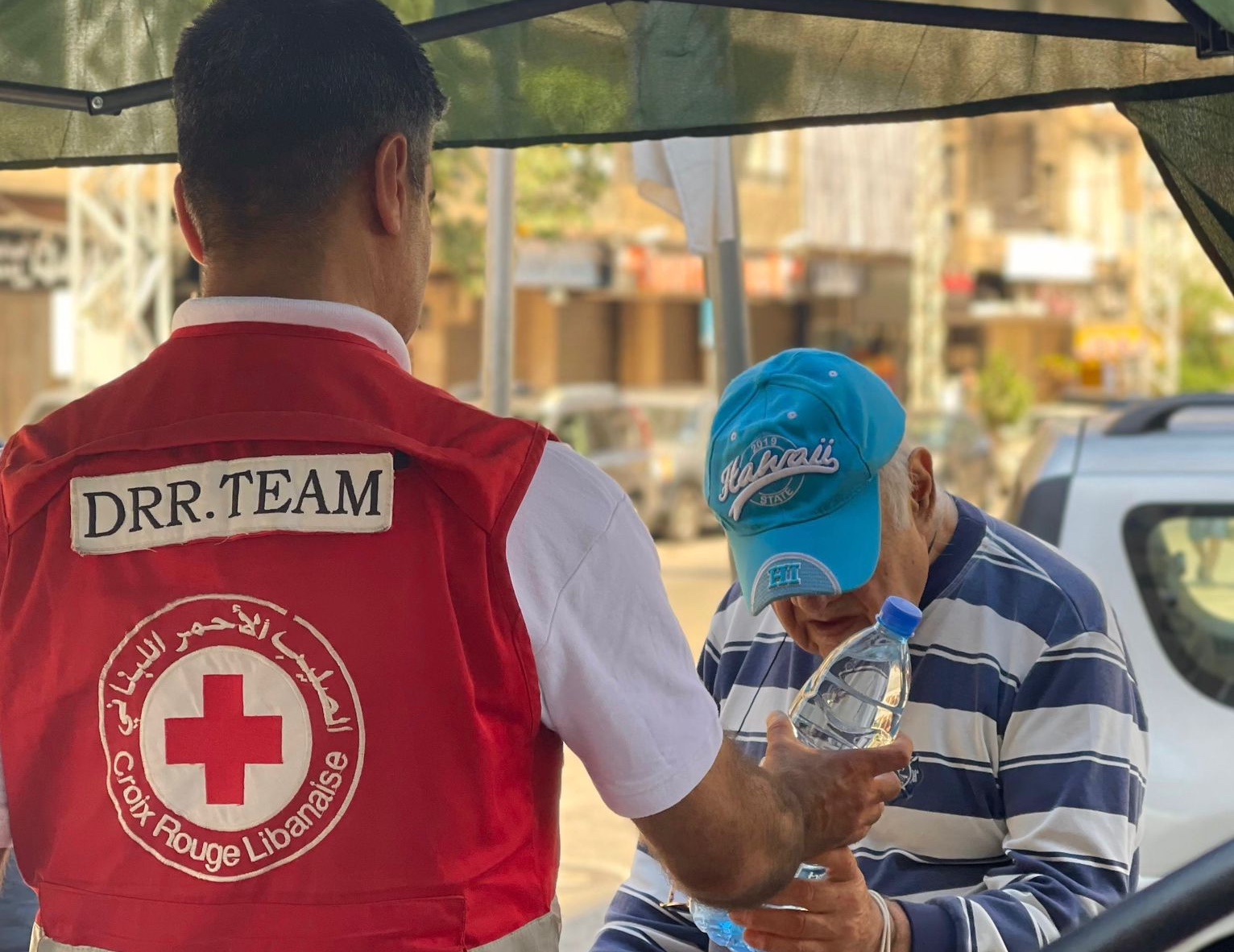 A member of the Lebanese Red Cross Disaster Risk Reduction team shares a water bottle with an elderly man as part of a comprehensive plan to get ahead of heatwave season.
