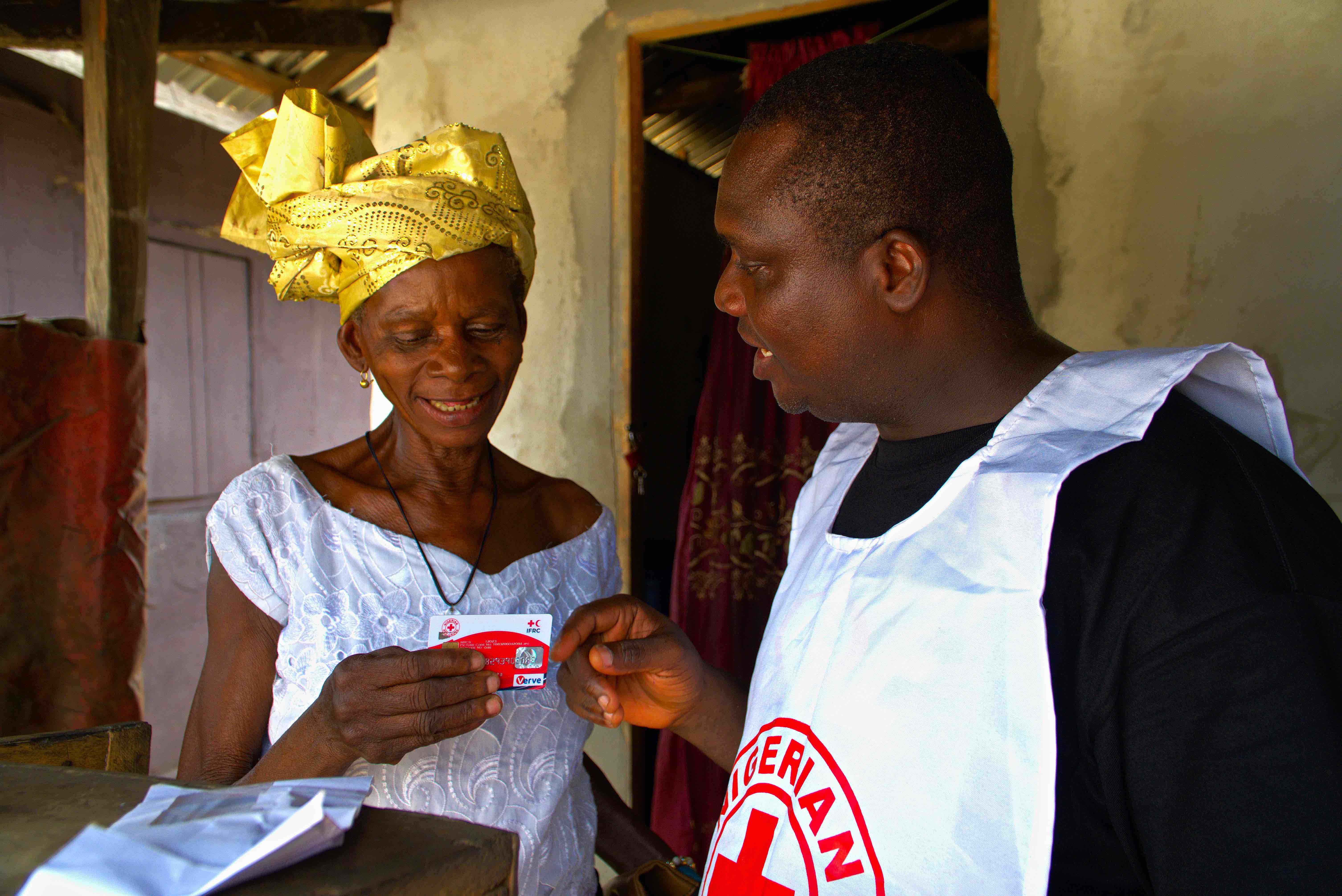 A volunteer with the Nigerian Red Cross provides a cash card to Miriam Abide, whose home was destroyed by the floods and then later rebuilt by the Nigerian 