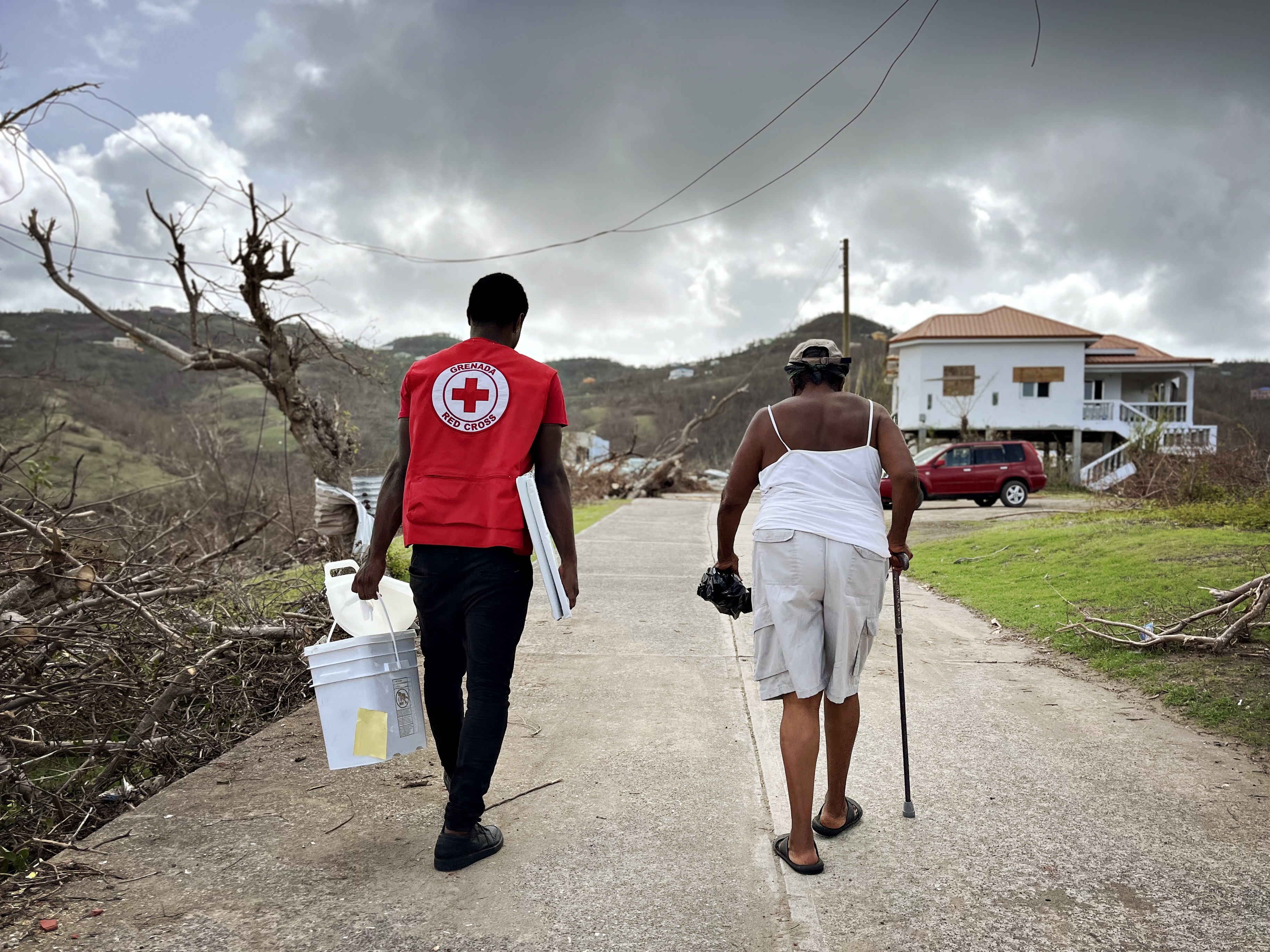 Un volontaire de la Croix-Rouge de Grenade porte un seau pour stocker de l'eau tout en marchant avec une femme locale dans une communauté touchée par l'ouragan Beryl.