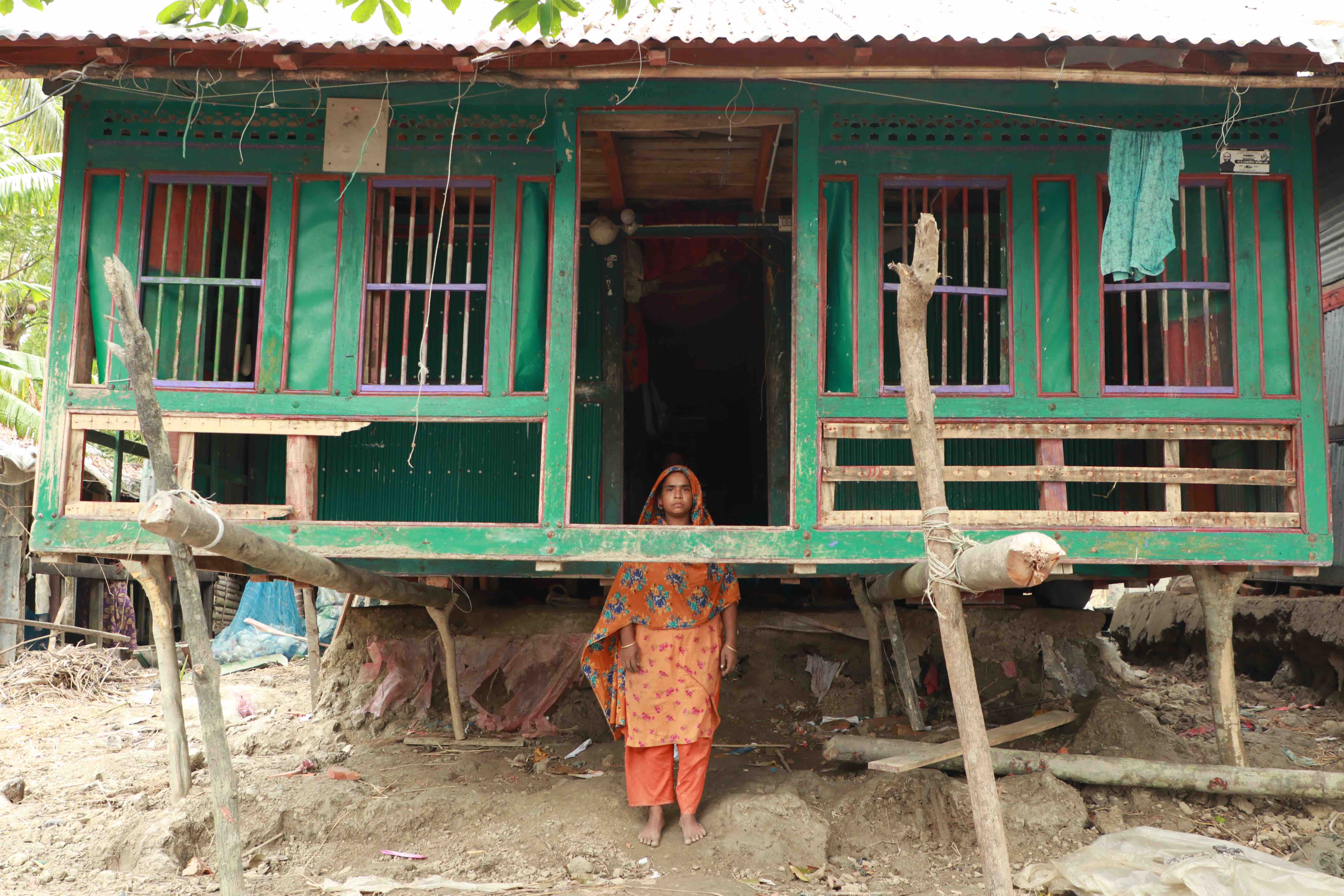 A woman stands in what used to be the foundation of her home, which was completely washed away by the storm and now is being held up by makeshift supports.