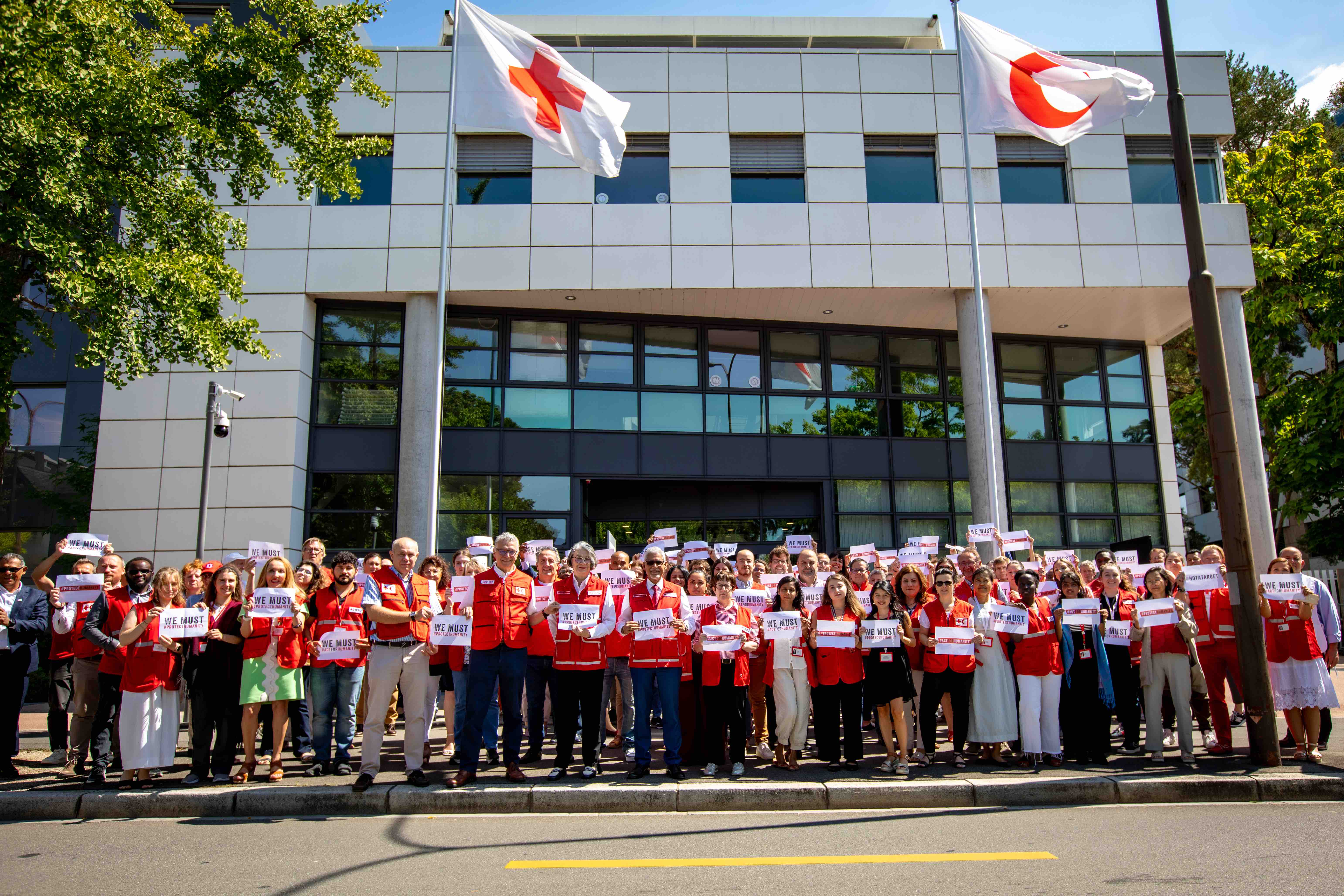 IFRC staff gather outside their headquarters in Geneva, Switzerland, holding signs saying 'We must Protect Humanity' as part of a global 'Stand in Solidarity' event demanding protection for humanitarian workers and volunteers.