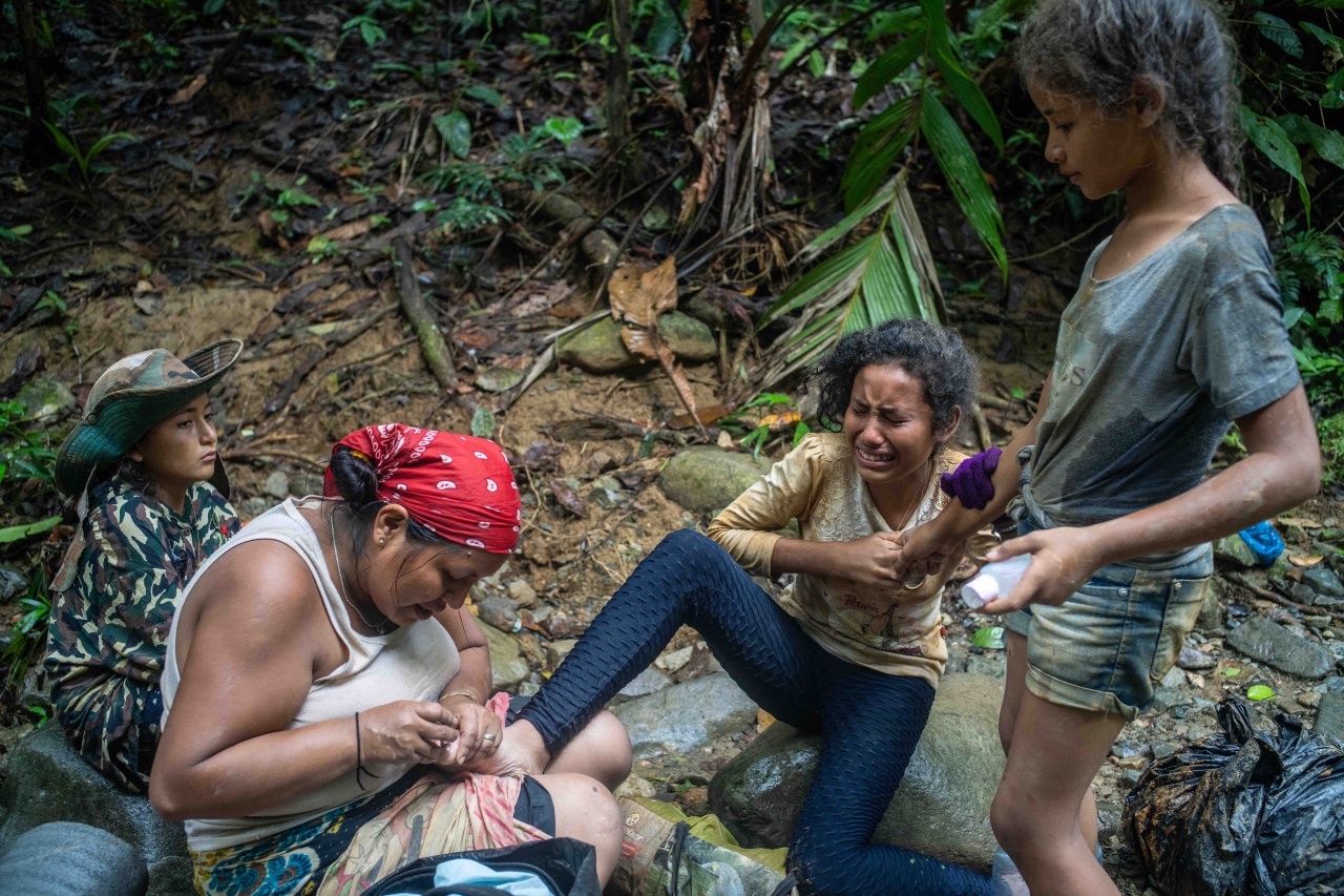 Jheymmi Bastidas tends to her stepdaughter Hamleisy's injured foot, offering comfort and care after several days of walking. With a look of pain on her face, Hamleisy is supported by her sisters, Adriannys and Hamleisky, who stand by her side.