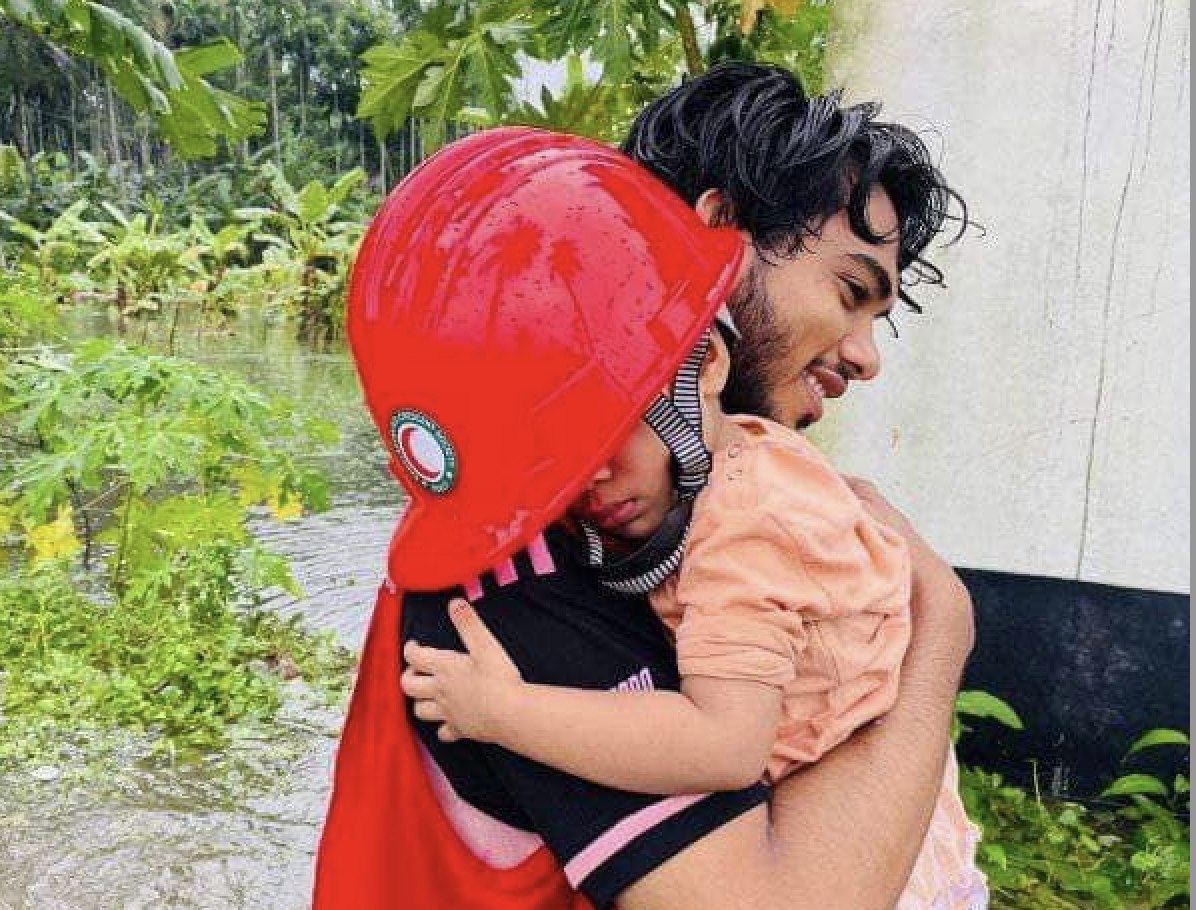 A Bangladesh Red Crescent volunteer carries a tired toddler through flood waters to safety.