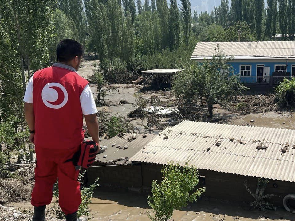 A volunteer with the Kyrgyszstan Red Crescent looks over extensive damage caused to a community by heavy flooding in June 2024.