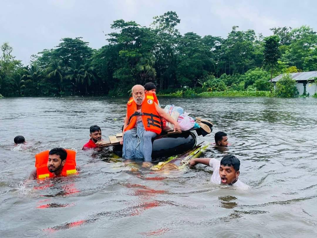 Bangladesh Red Crescent volunteers use a makeshift raft to carry several people through shoulder-height flood waters.
