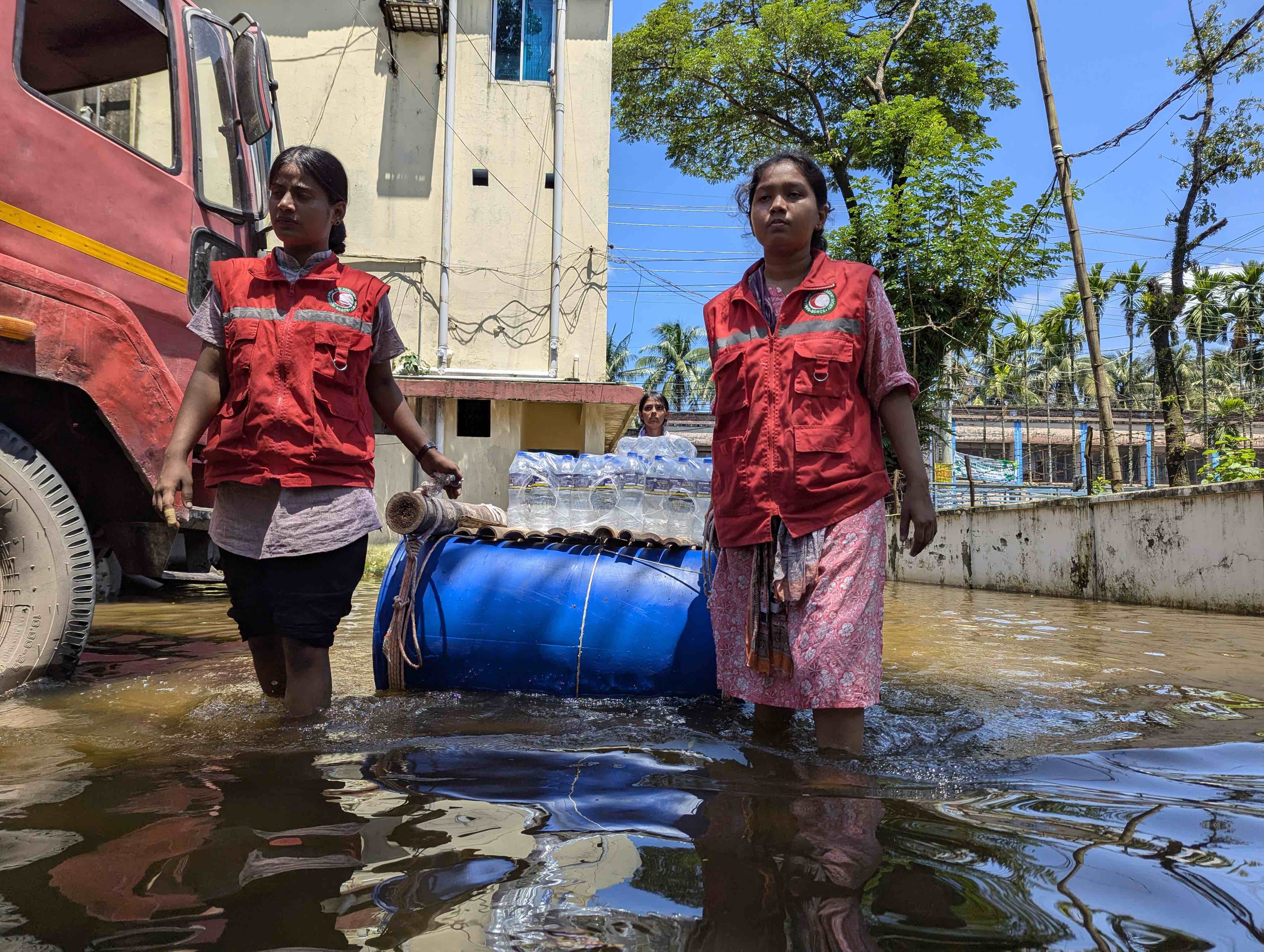 Two Bangladesh Red Crescent volunteers use a flotation device to carry cases of bottled water to people impacted by sudden, severe flooding.