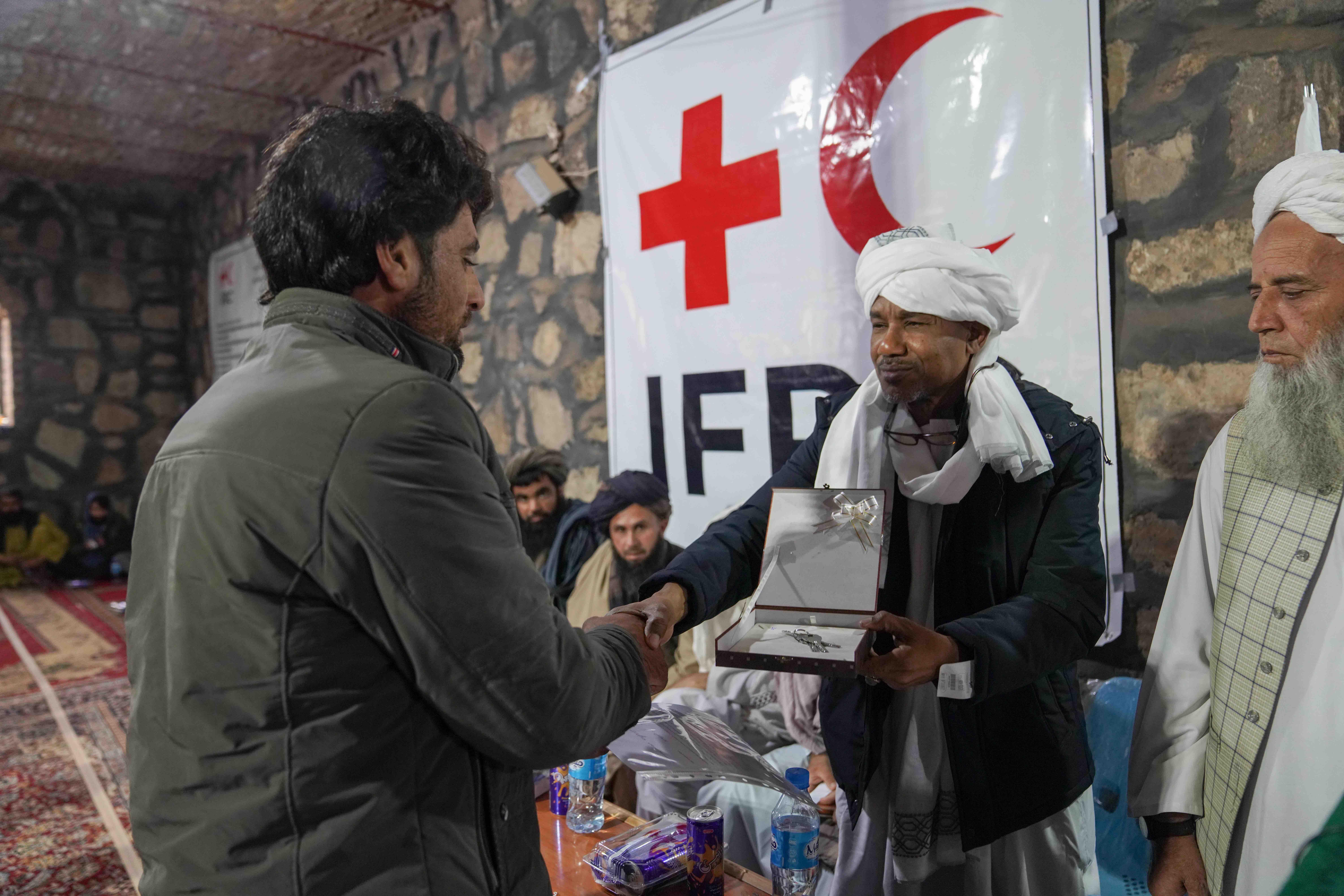 An IFRC staff member hands over the keys of a newly constructed shelter to one of the families impacted by the October 2023 earthquakes during a shelter handover ceremony in November.